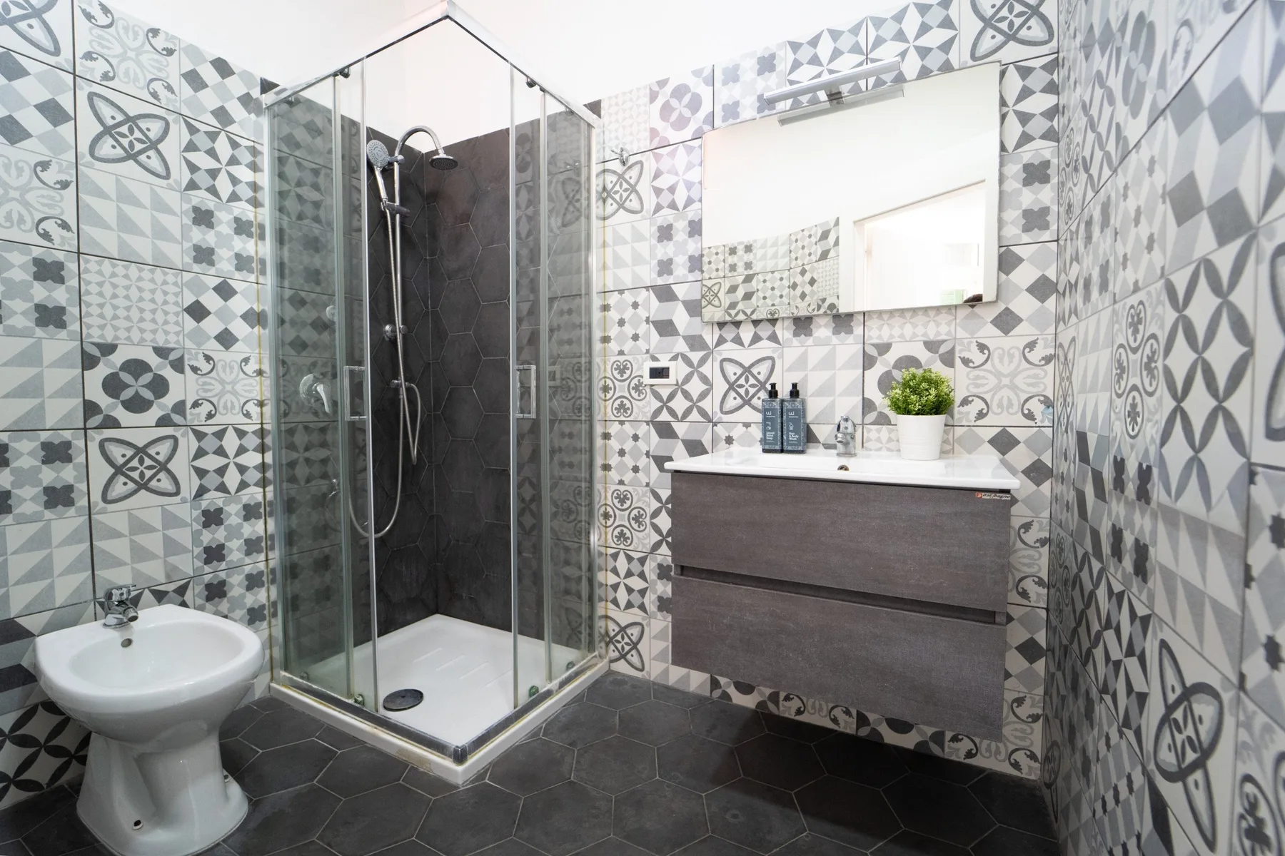 A tiled bathroom with a glass shower, sink, and wall-mounted vanity.