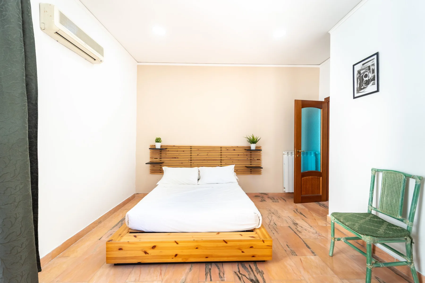 A bright bedroom with a bed, wooden headboard, and a green chair.
