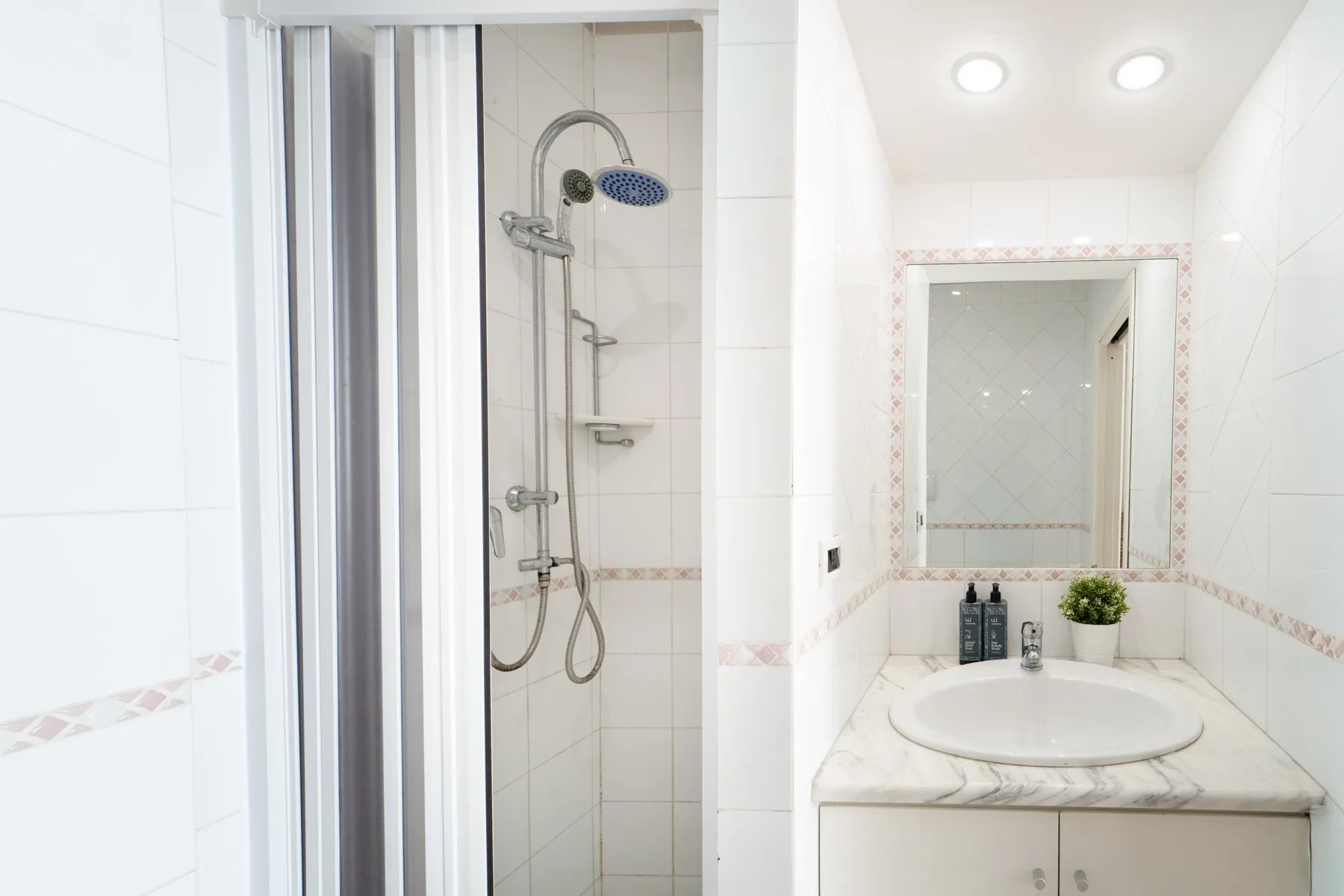 A tiled bathroom with a shower and a sink beneath a mirror.