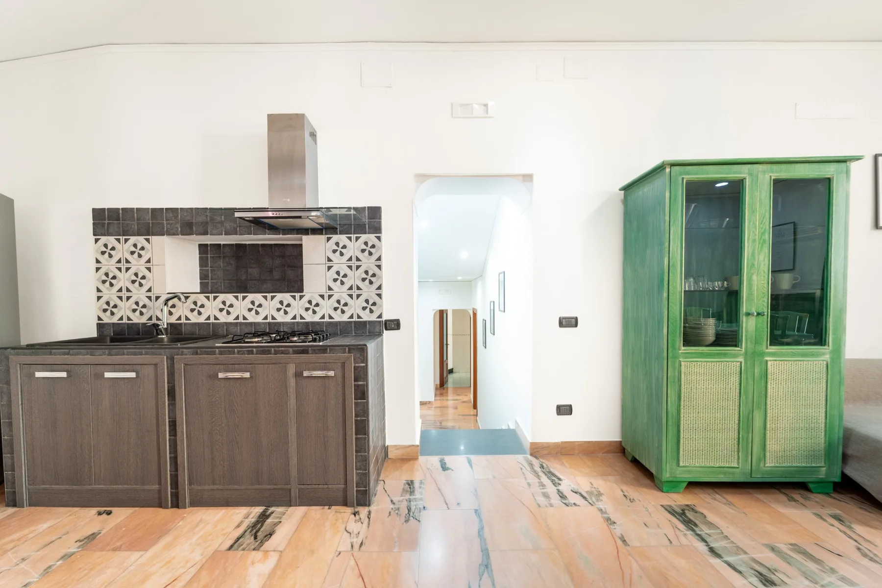 A kitchen area with dark cabinets, patterned backsplash, and a green glass-front cabinet.
