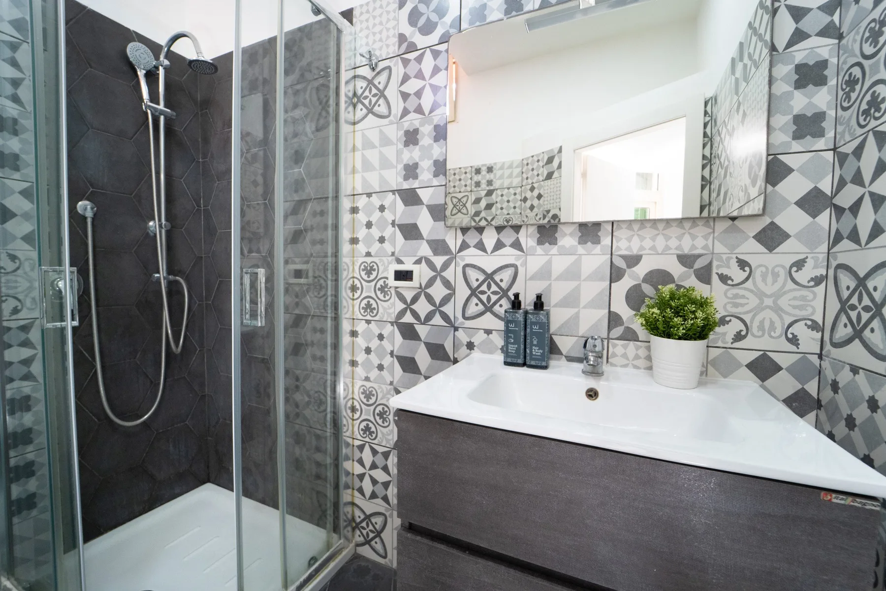 A bathroom with a glass shower and a sink vanity against patterned tile.