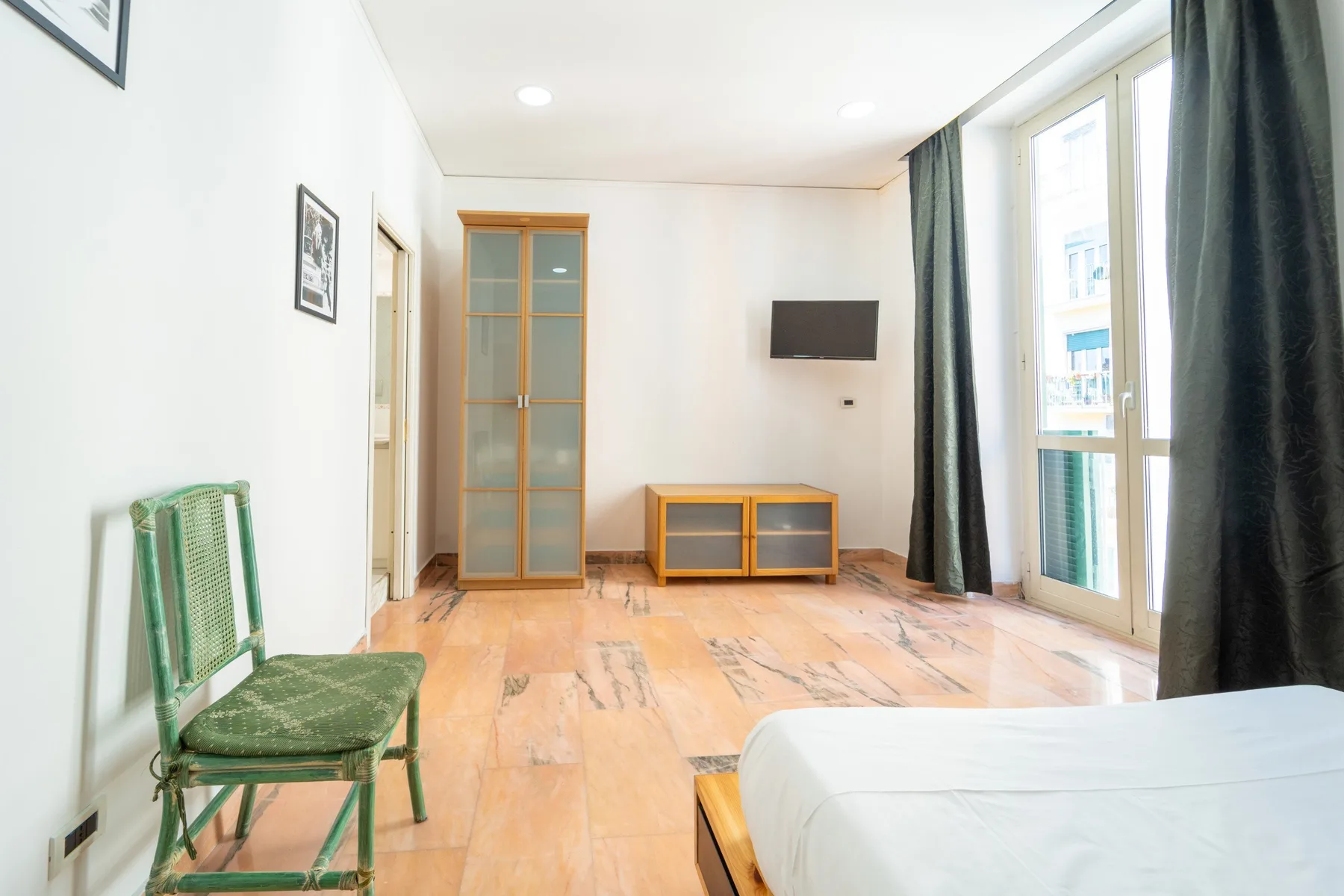 A bright bedroom with a bed, green seating, and a wall-mounted television.