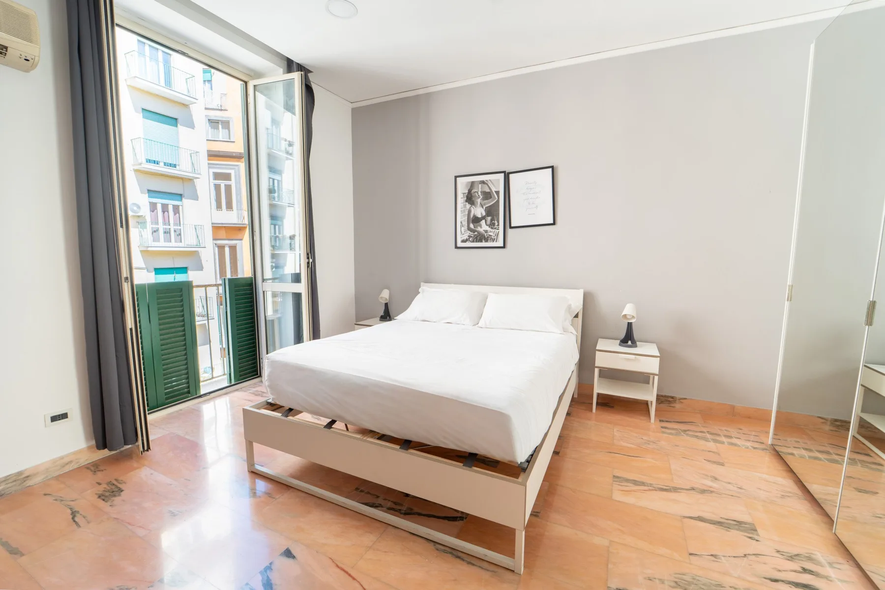 A bright bedroom with a neatly made bed beside tall windows.
