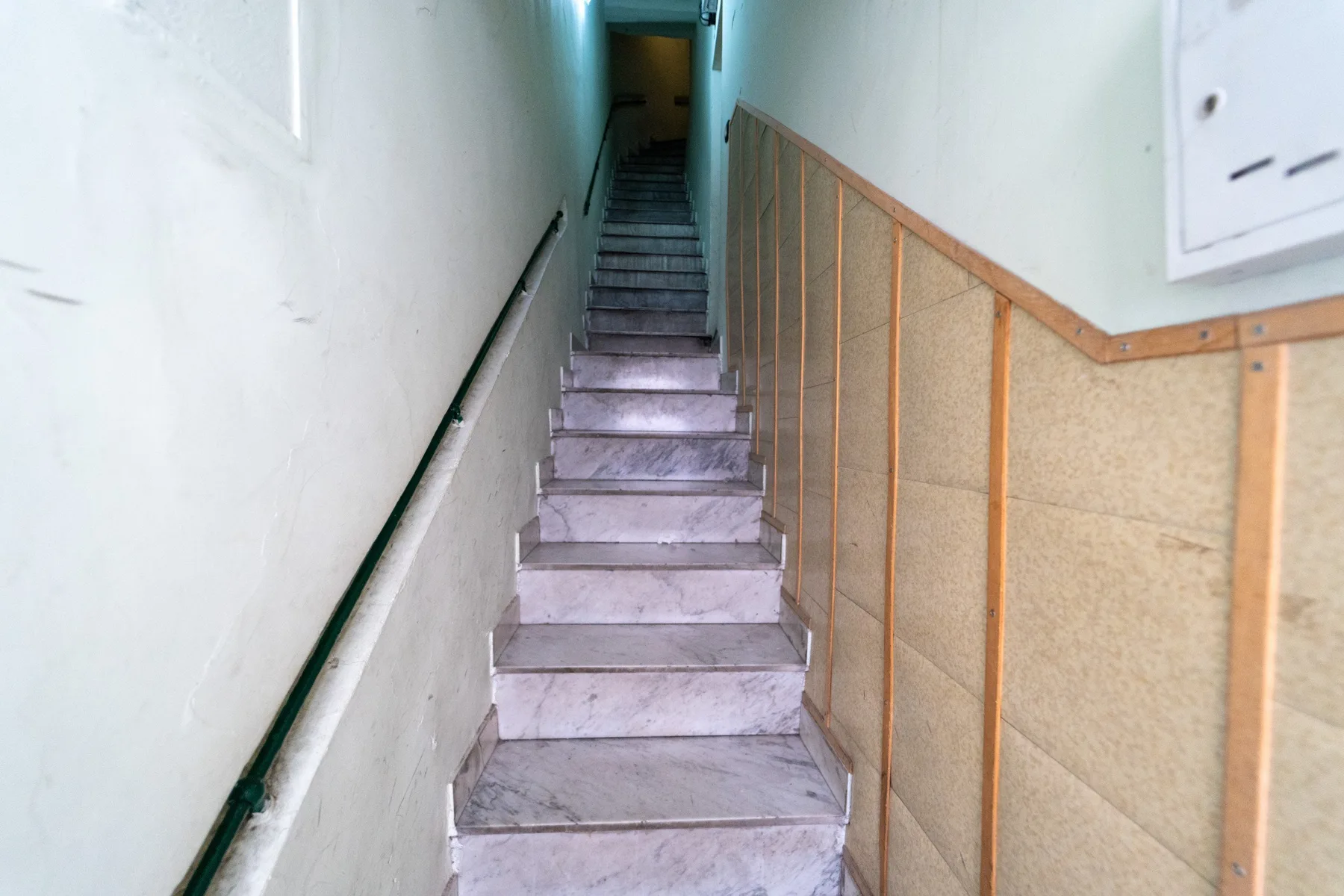 A narrow indoor stairwell with steps leading upward and a handrail along the wall.