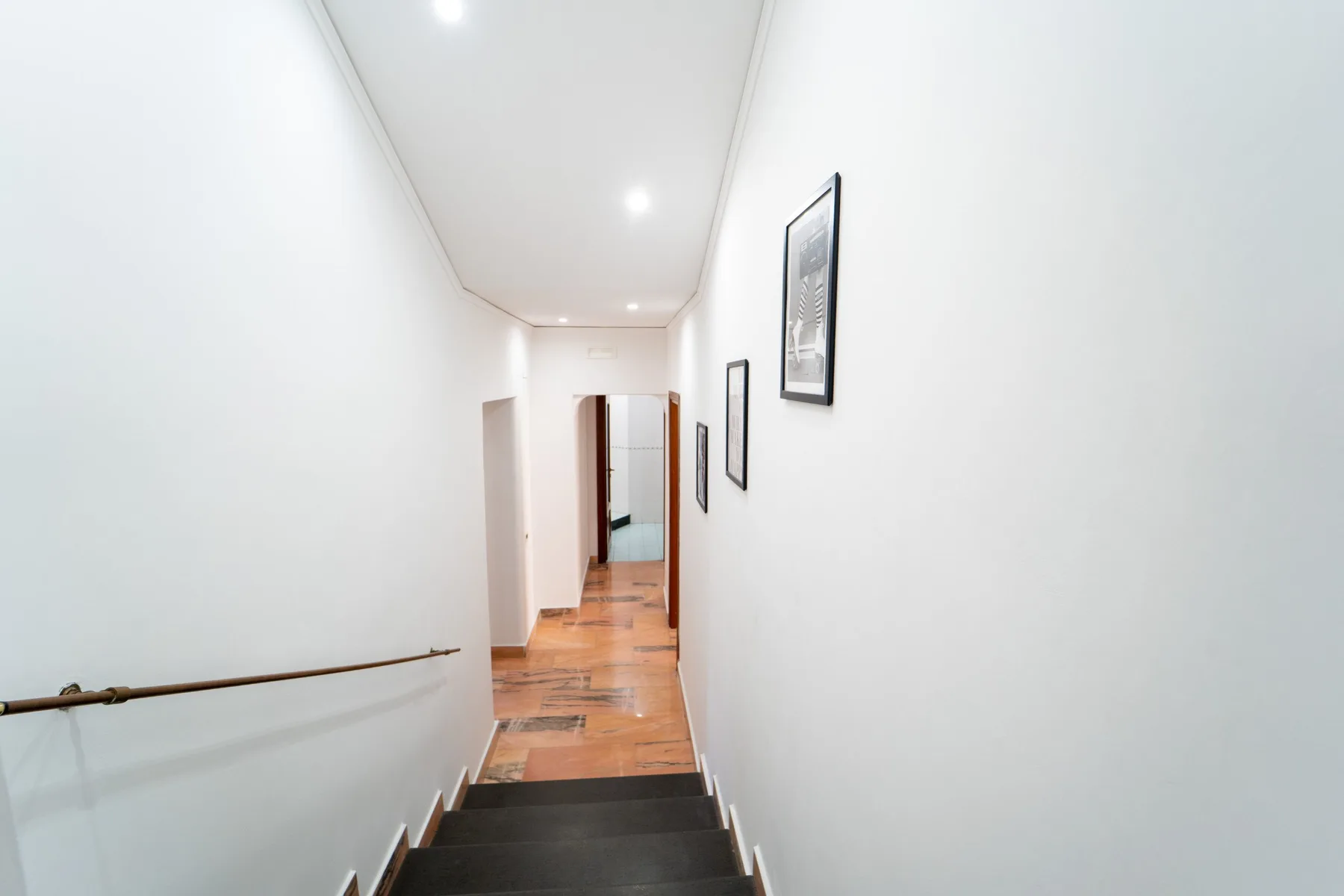 A bright interior hallway has framed pictures along the wall and stairs in the foreground.
