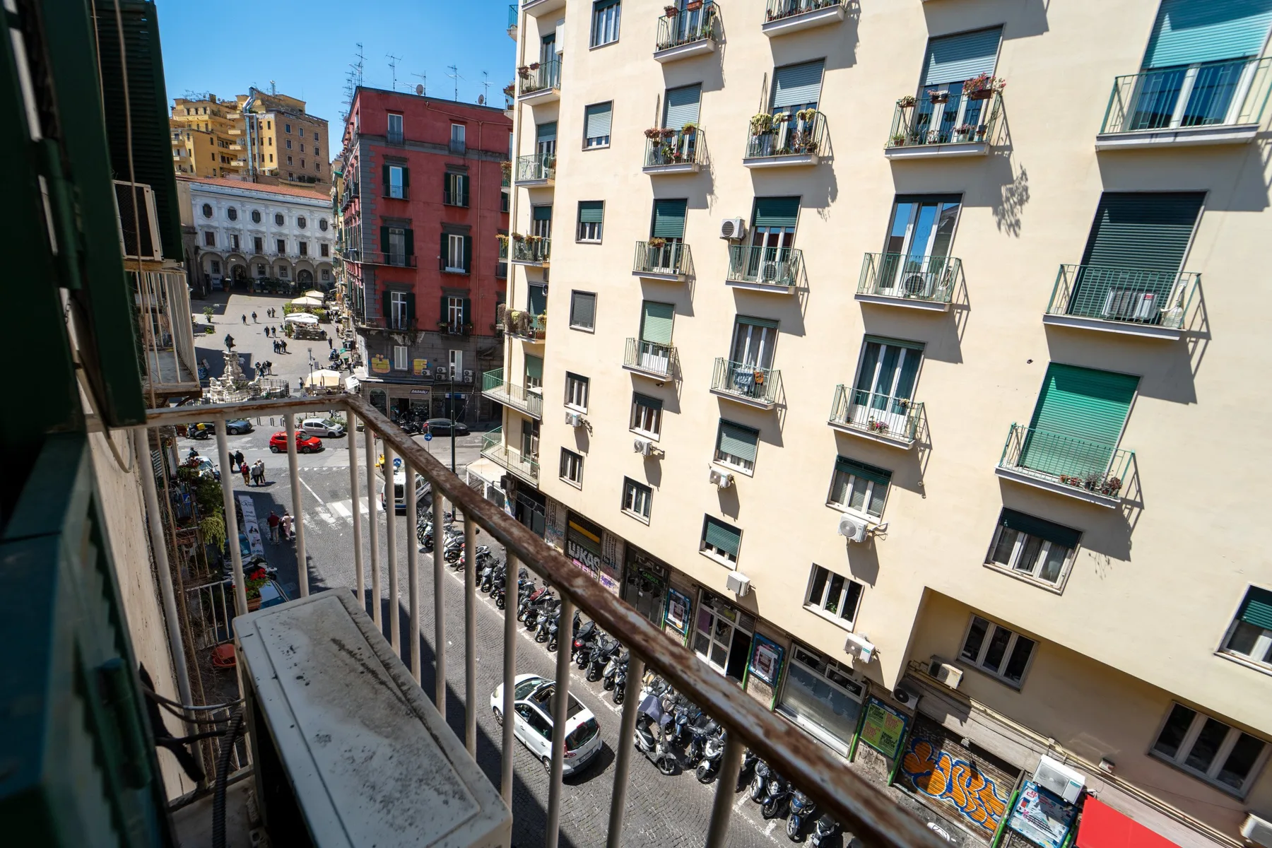 A balcony overlooks a city street lined with apartment buildings.