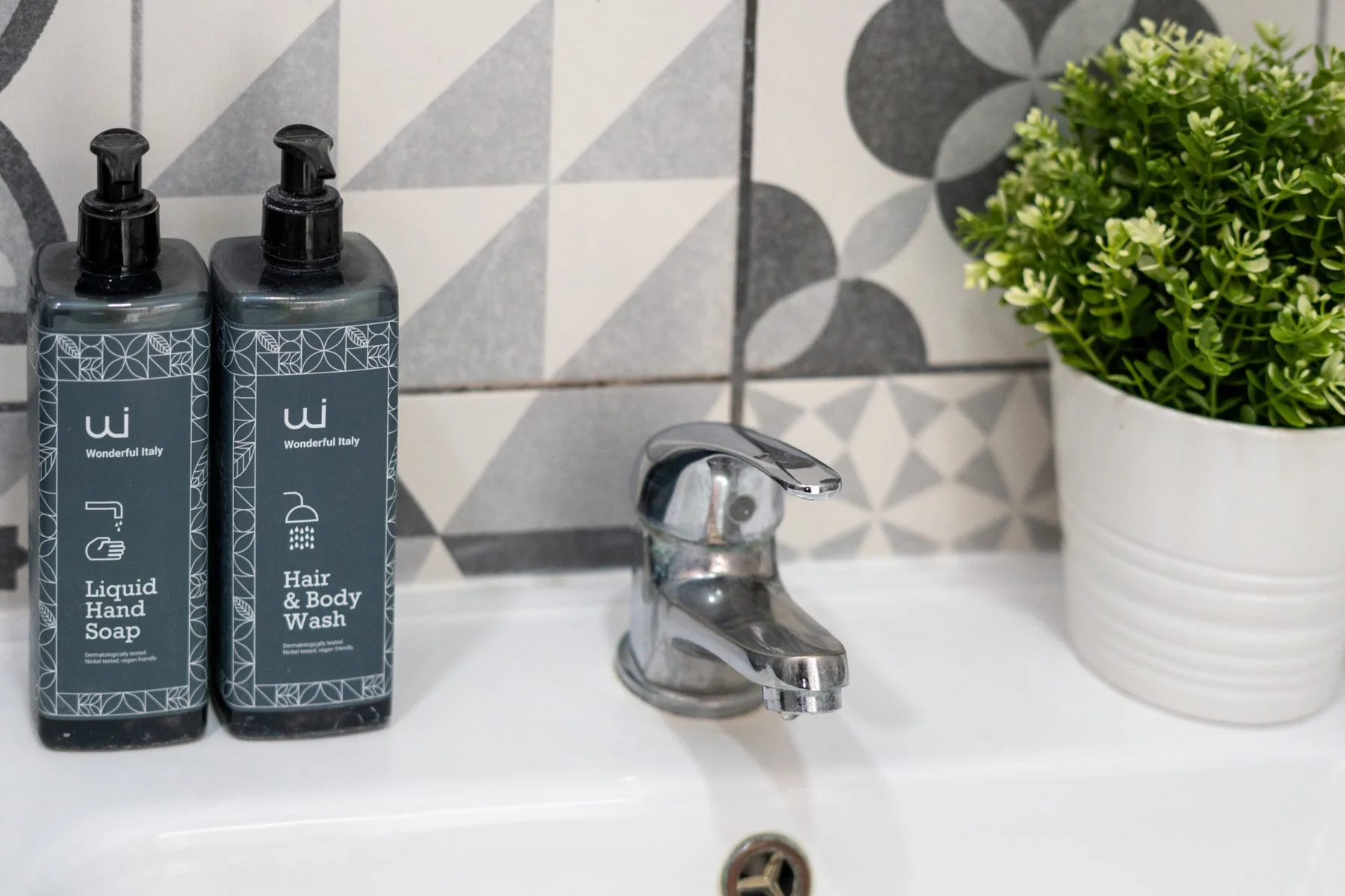 A bathroom sink with a chrome faucet, soap dispensers, and a potted plant.