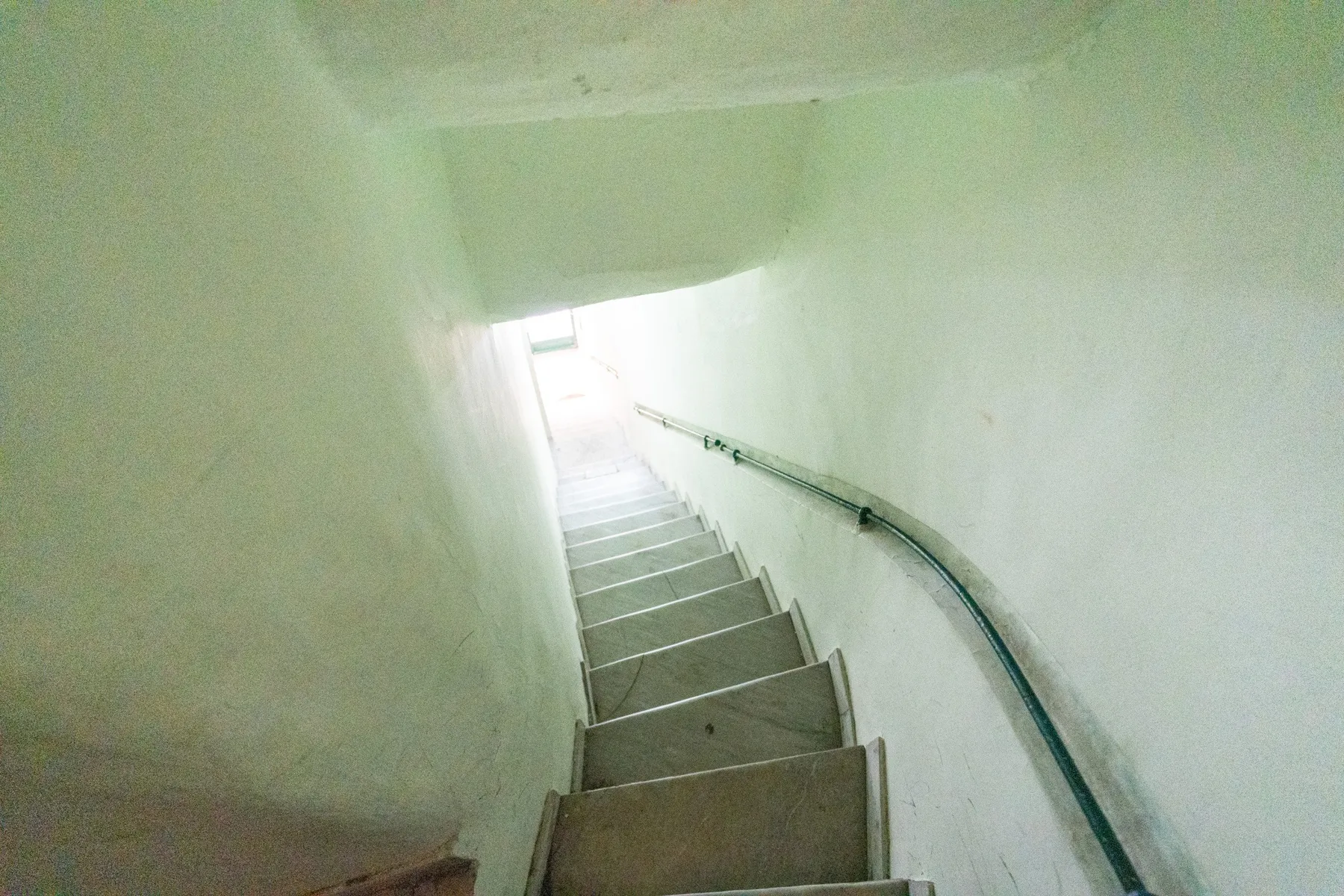 A narrow stairwell descends toward a bright opening, with a handrail along the wall.