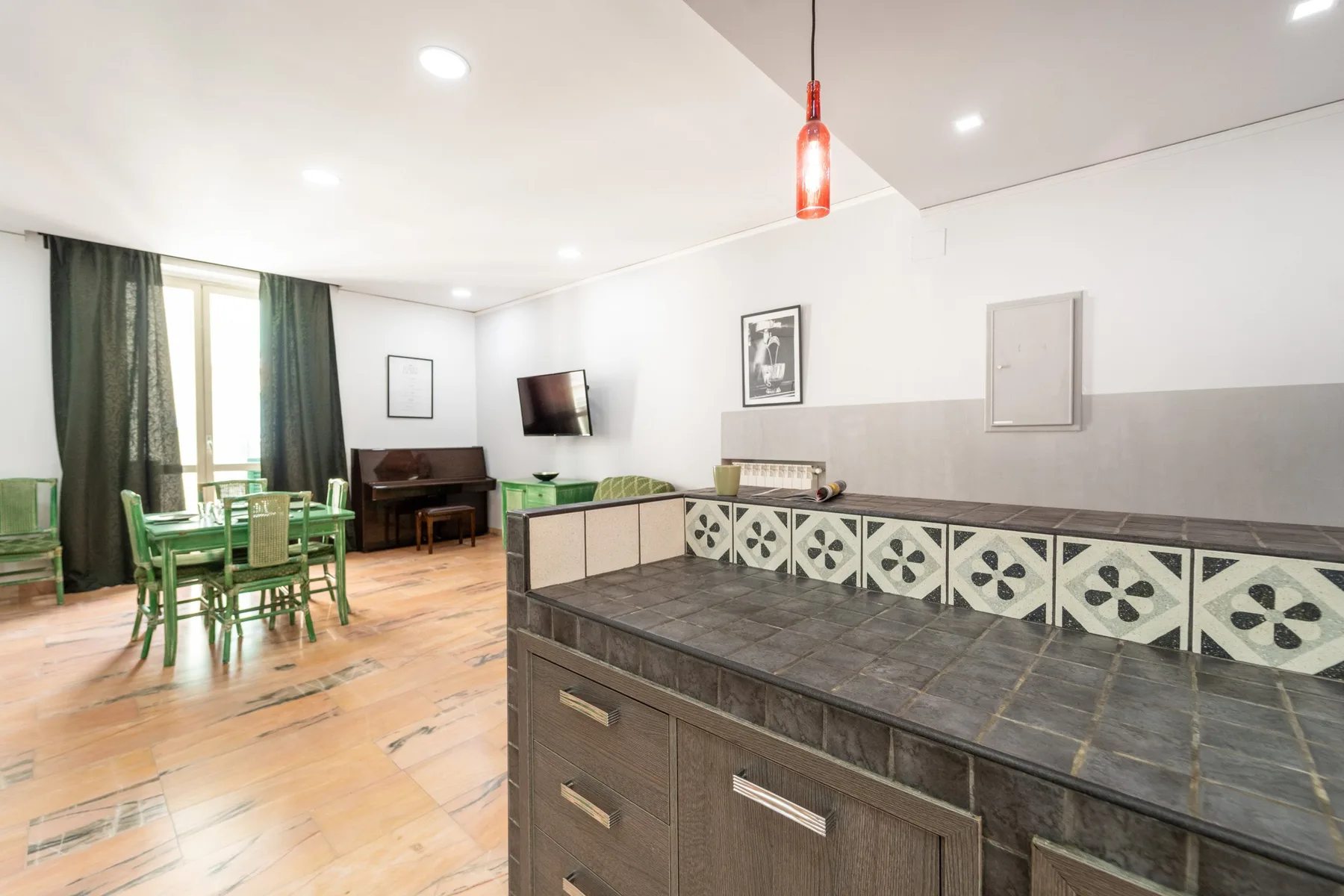 A bright living and dining area with green seating and a long tiled counter.