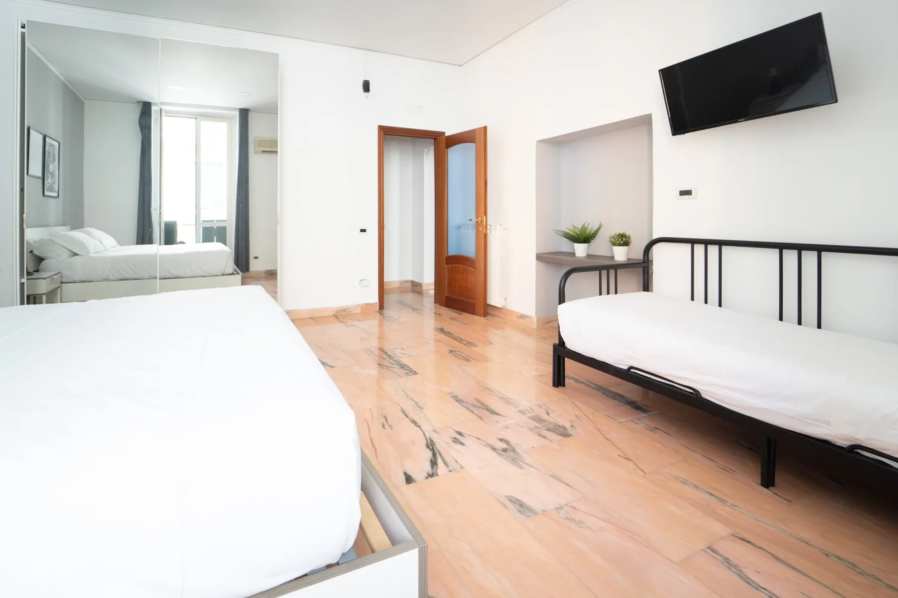 A bright bedroom with beds, mirrored closet doors, and an open wooden door.