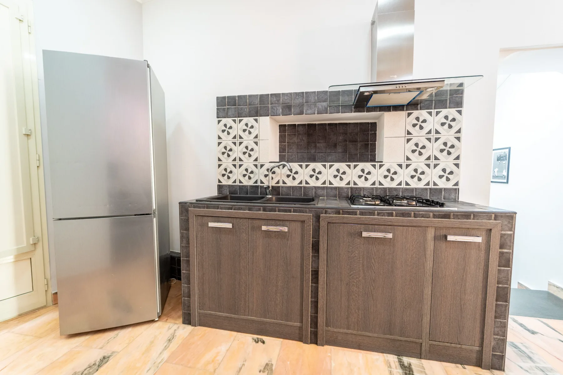 A kitchen with dark cabinetry, a tiled backsplash, and a refrigerator.