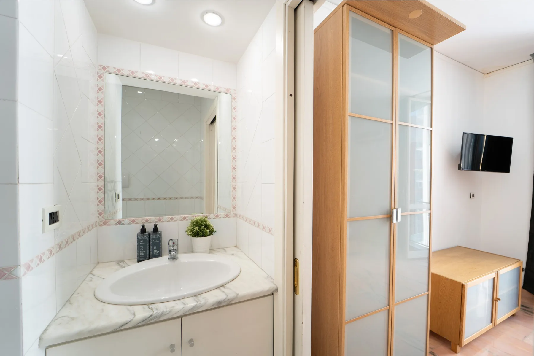 A bright bathroom vanity with a round sink stands beside a frosted glass partition.