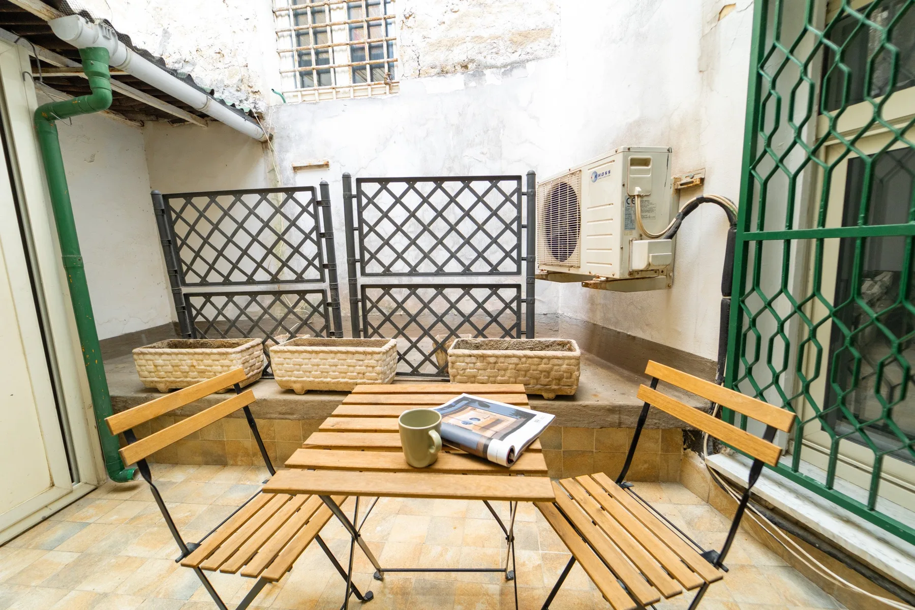 A small tiled patio with wooden seating and a metal lattice gate.
