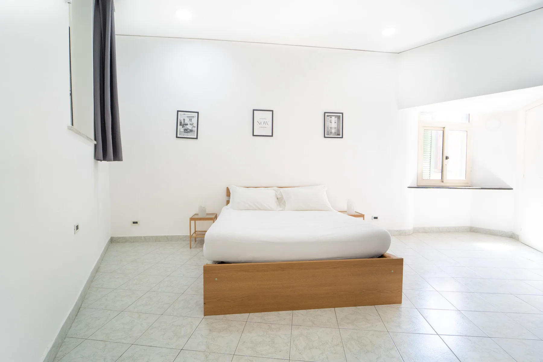 A bright bedroom with a bed, bedside tables, and windows.