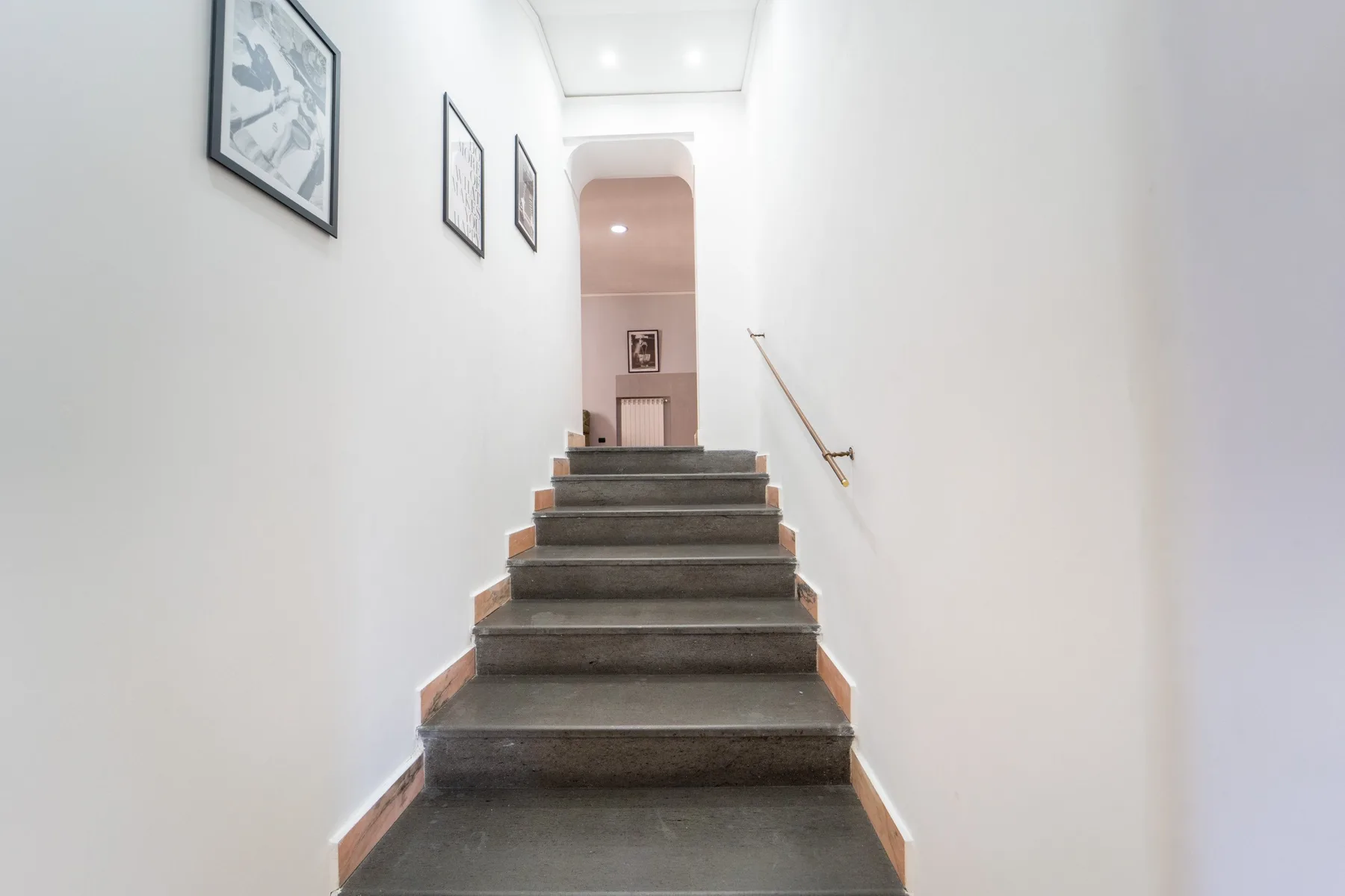 A staircase rises toward an arched doorway, with framed pictures on the wall.