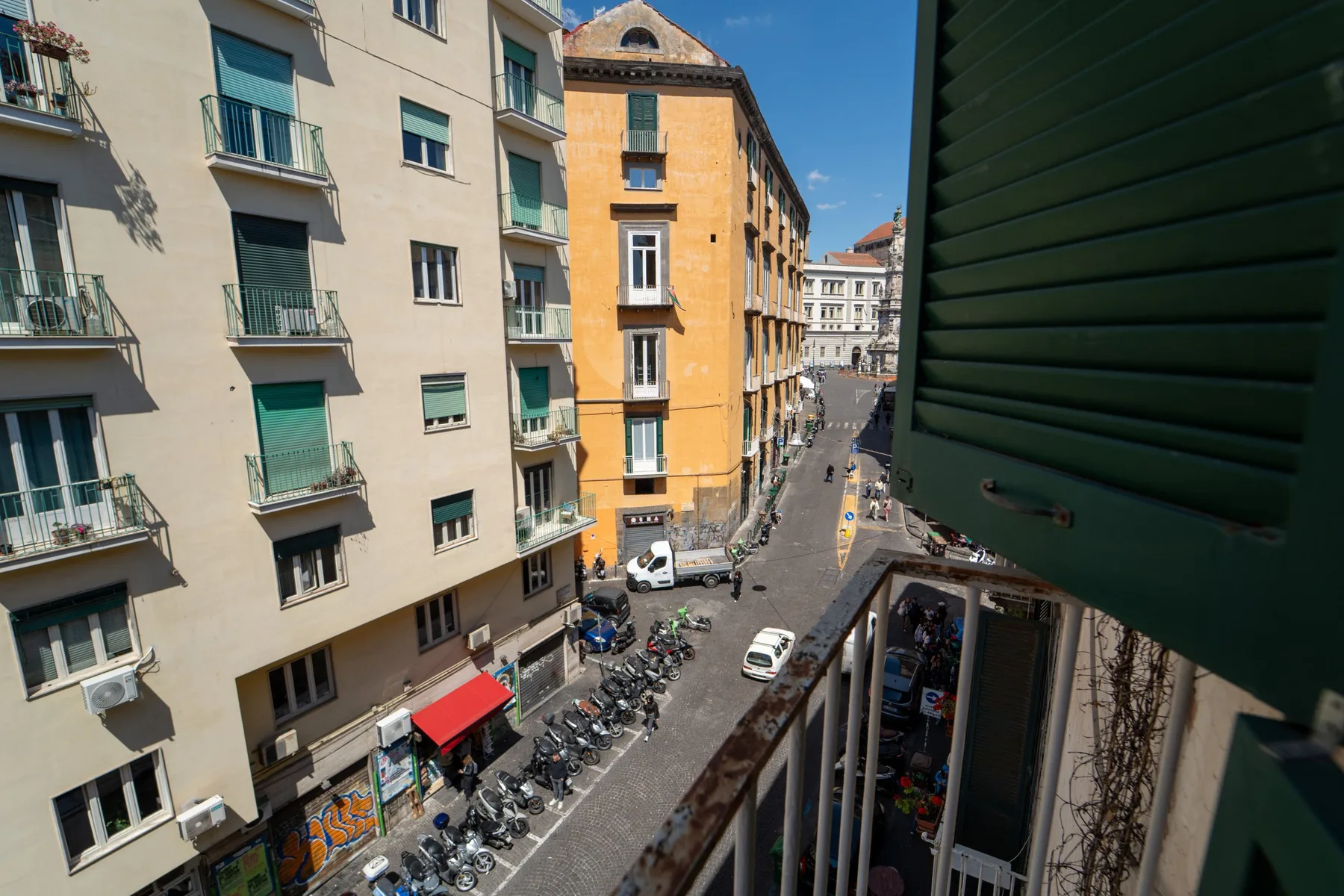 A city street viewed from above, lined with apartment buildings and parked scooters.