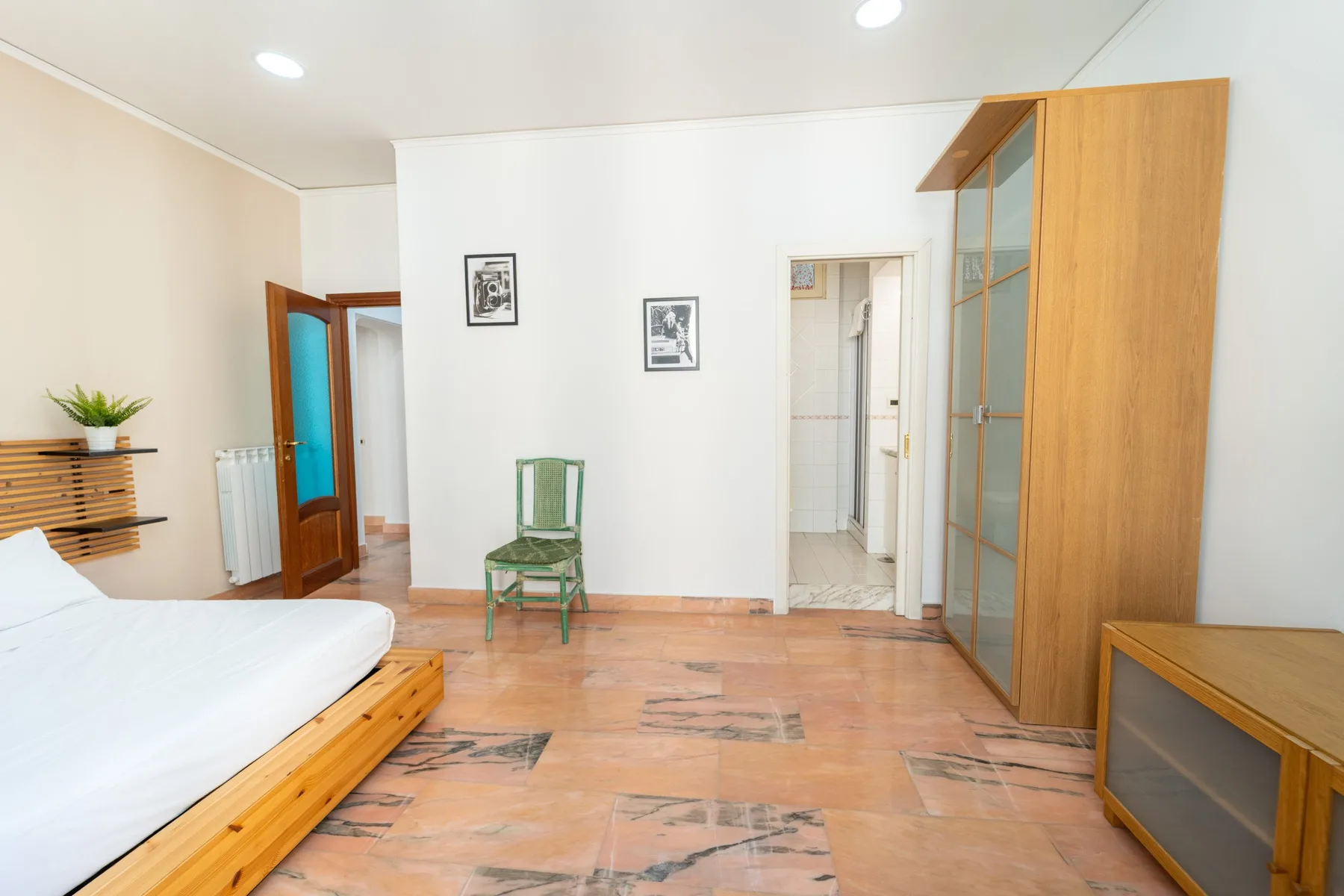 A bright bedroom with a bed, a green chair, and wooden flooring.