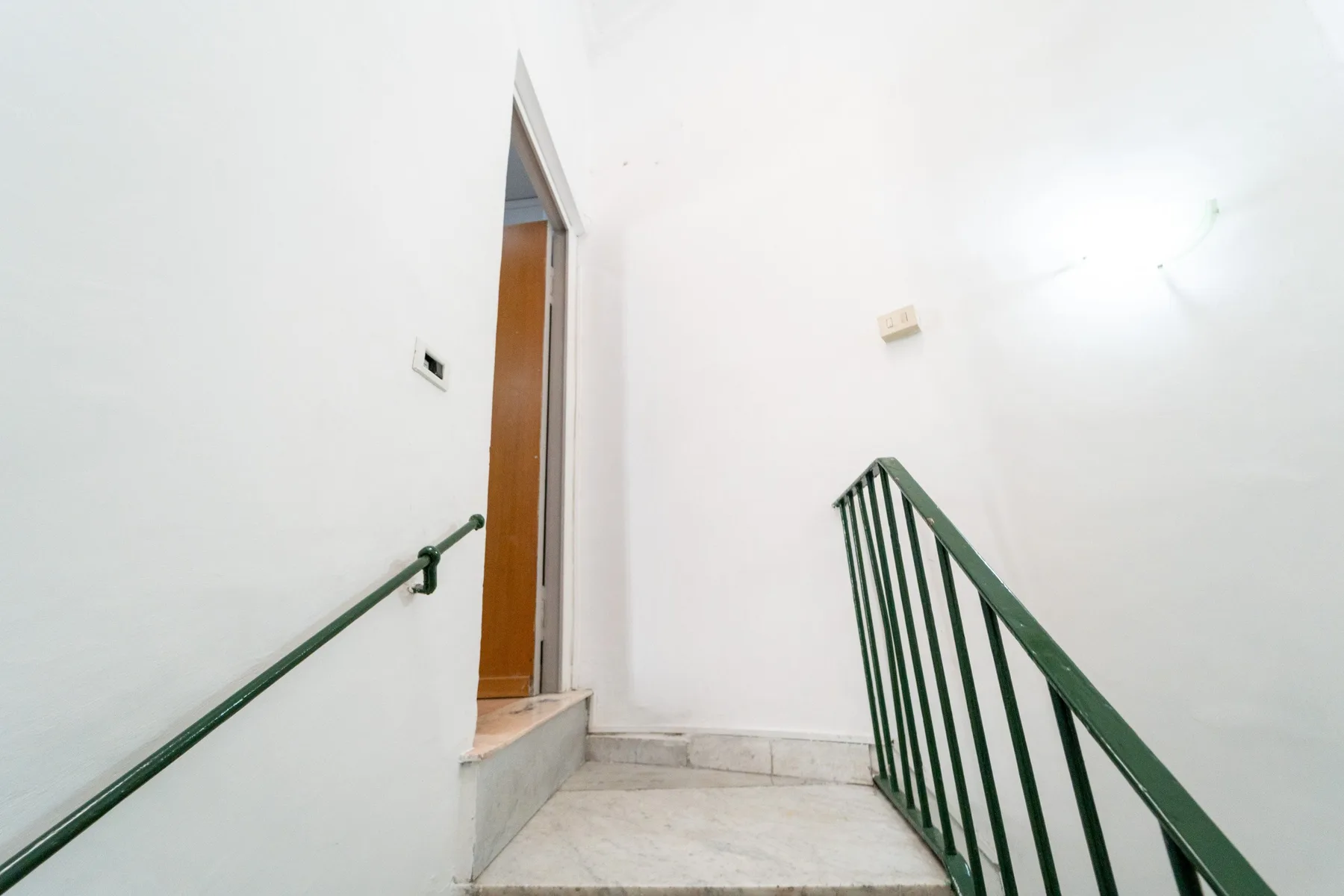 A small stair landing with green metal railings and an open doorway.