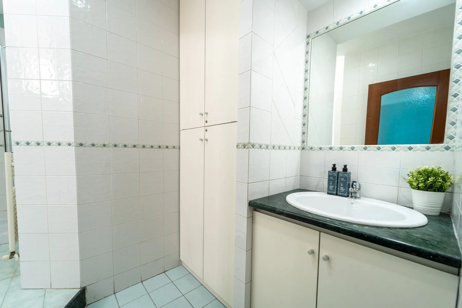 A tiled bathroom with a sink, mirror, and white storage cabinets.