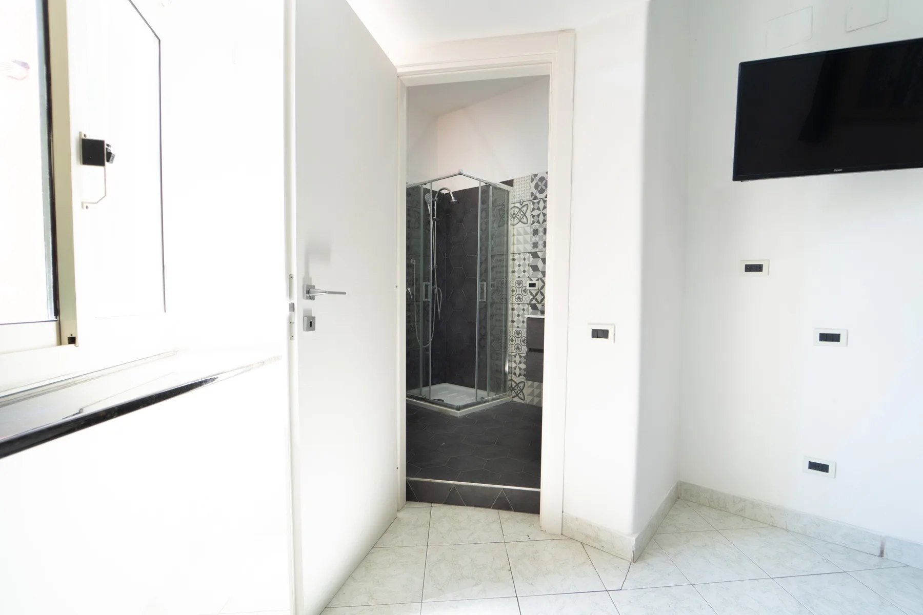 A bright bathroom entrance opens onto a glass shower with patterned tile.