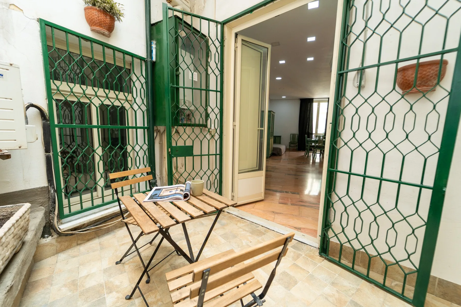 A small tiled patio with wooden seating and open green metal gates.
