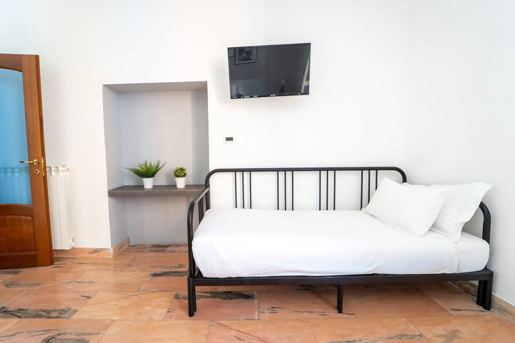 A bedroom with a white bed, black metal headboard, and wall-mounted television.