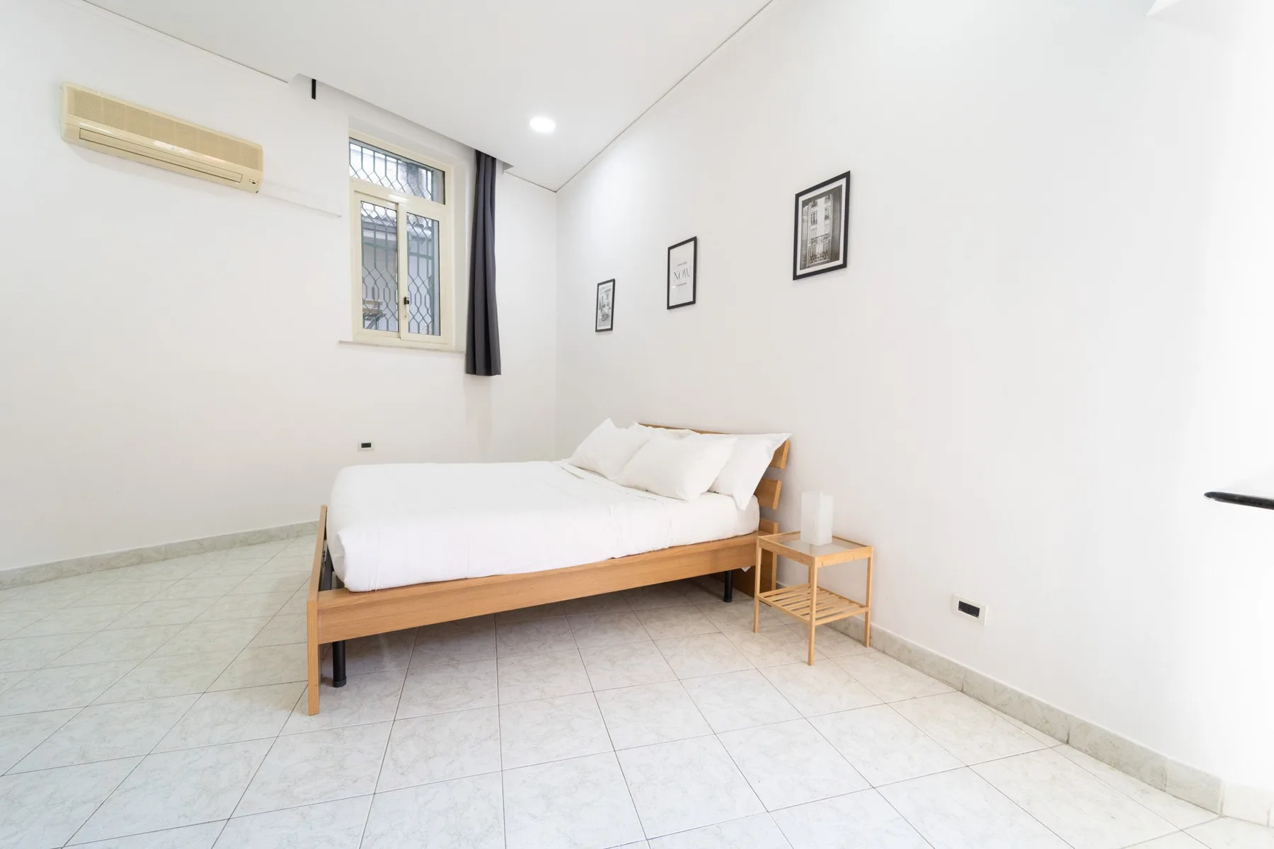 A bright bedroom with a neatly made bed and framed pictures on the wall.