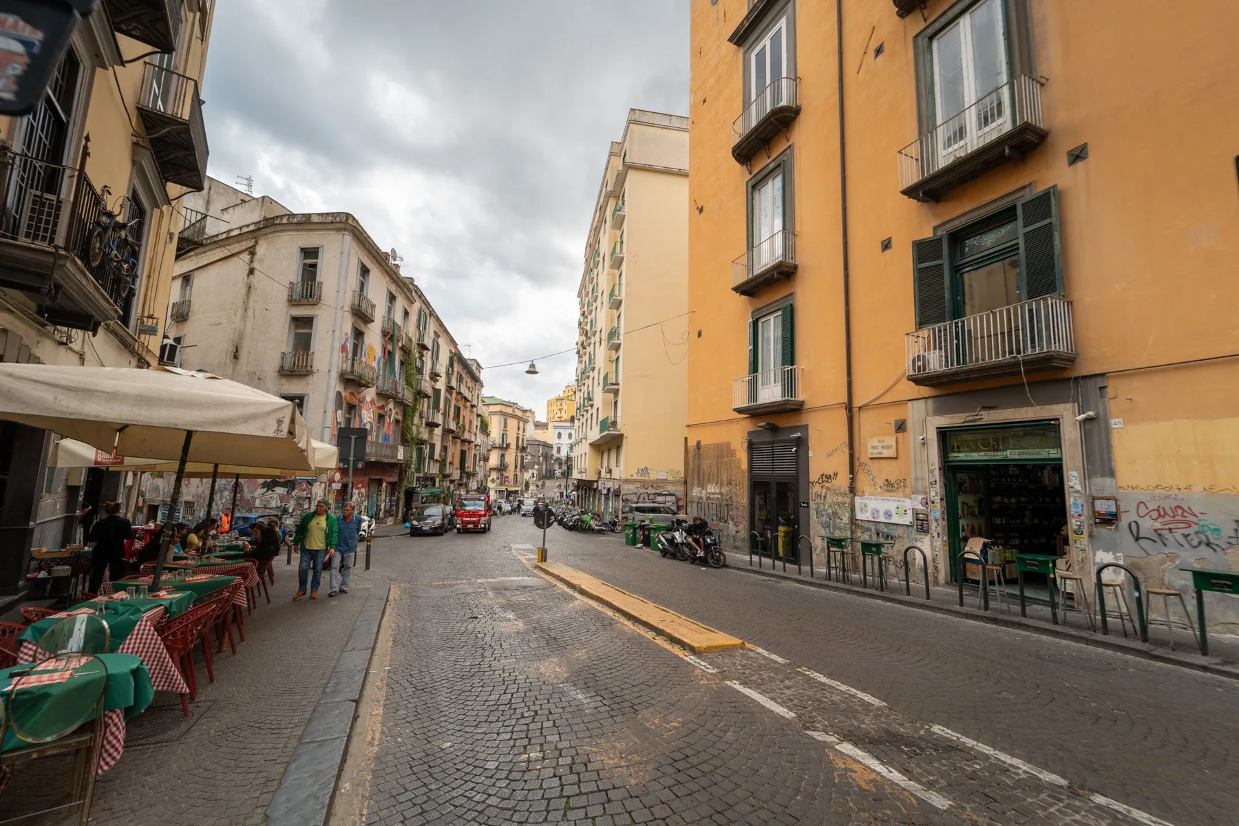 A cobblestone street lined with buildings and outdoor café seating.