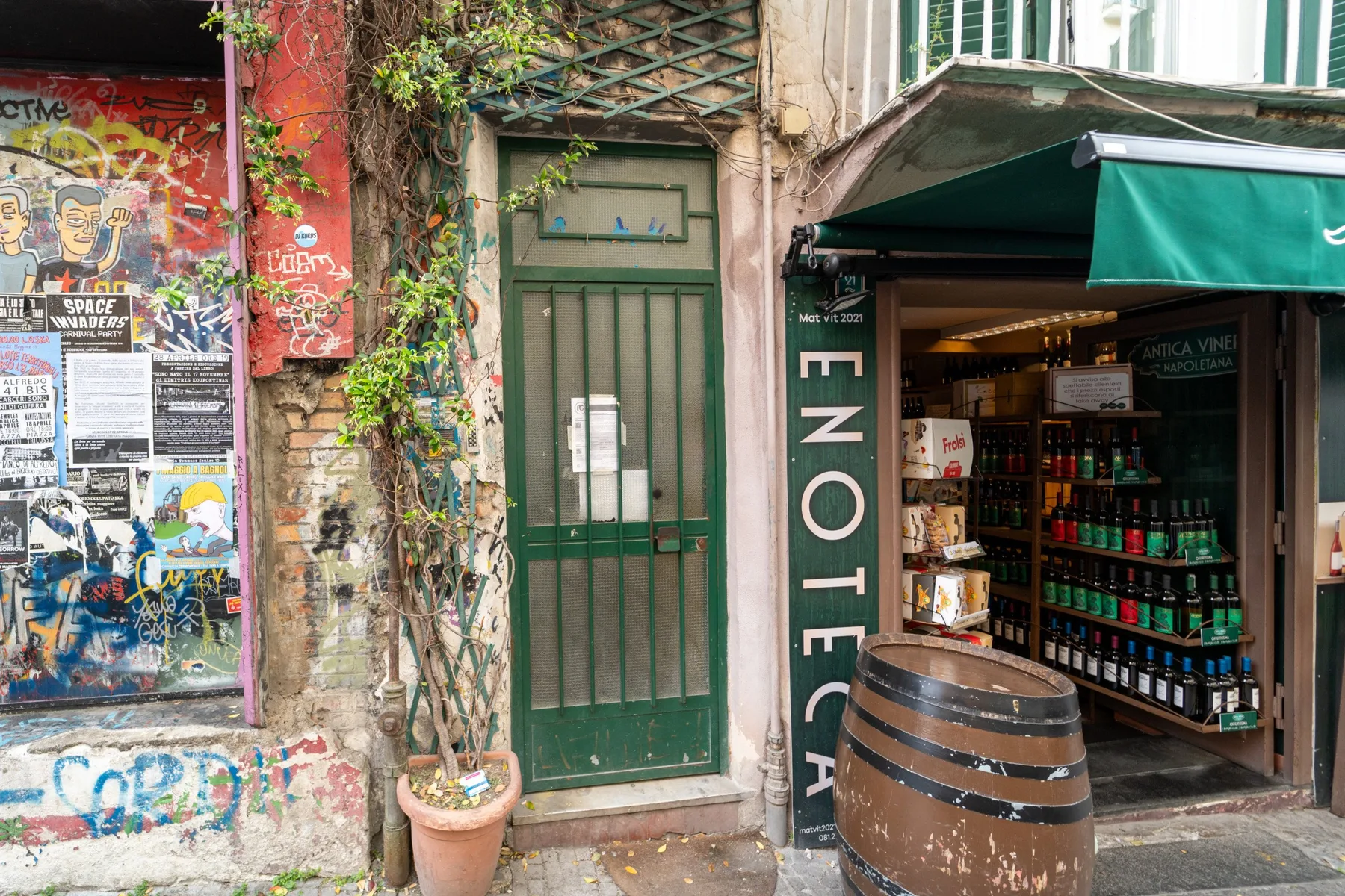 A narrow storefront entrance with a green door, awning, and display shelves.