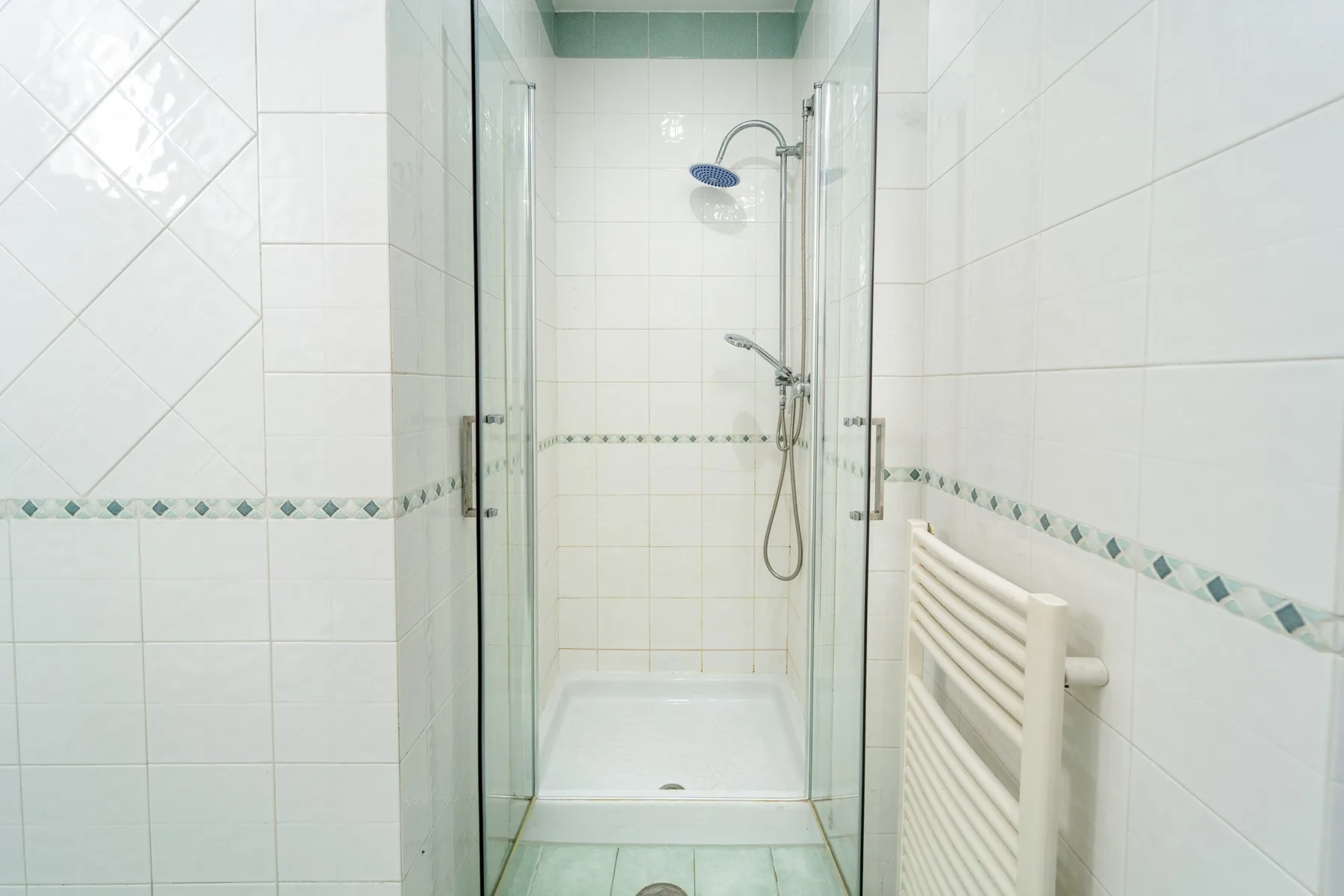 A tiled bathroom with a glass shower and a wall-mounted towel radiator.