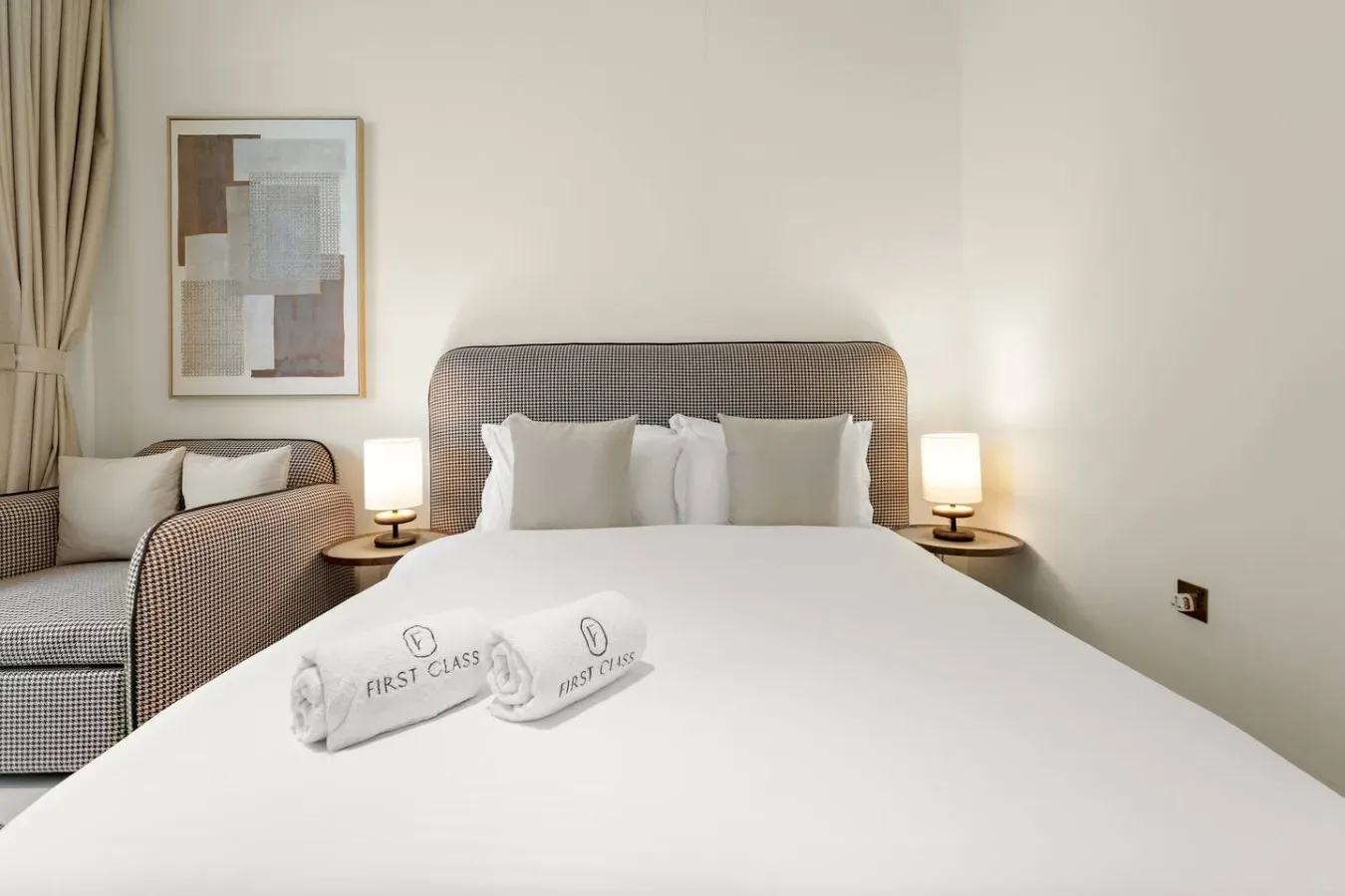 Un dormitorio luminoso con una cama bien tendida y una zona de estar al lado.
