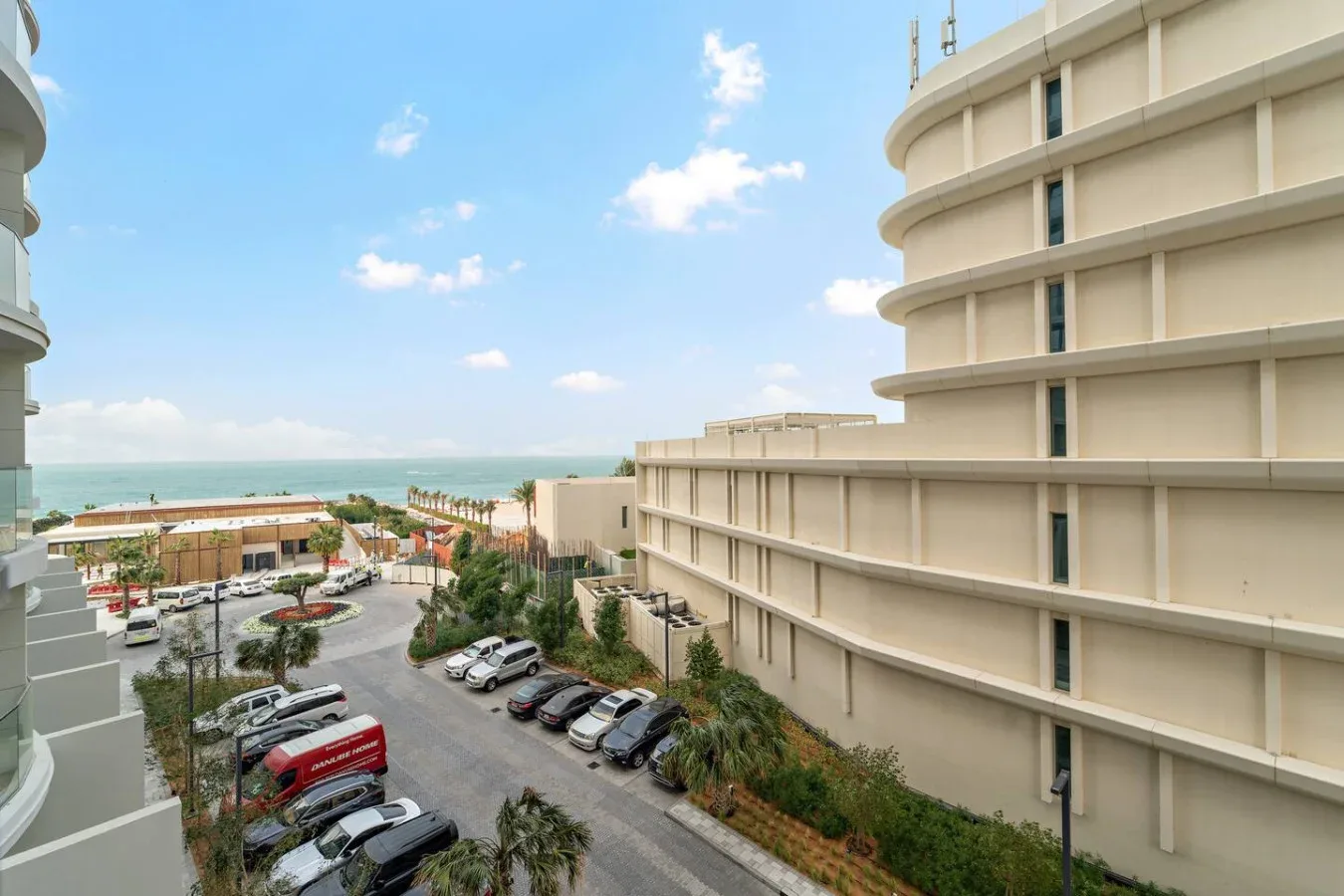 Una vista costera entre edificios da a un estacionamiento y al mar.