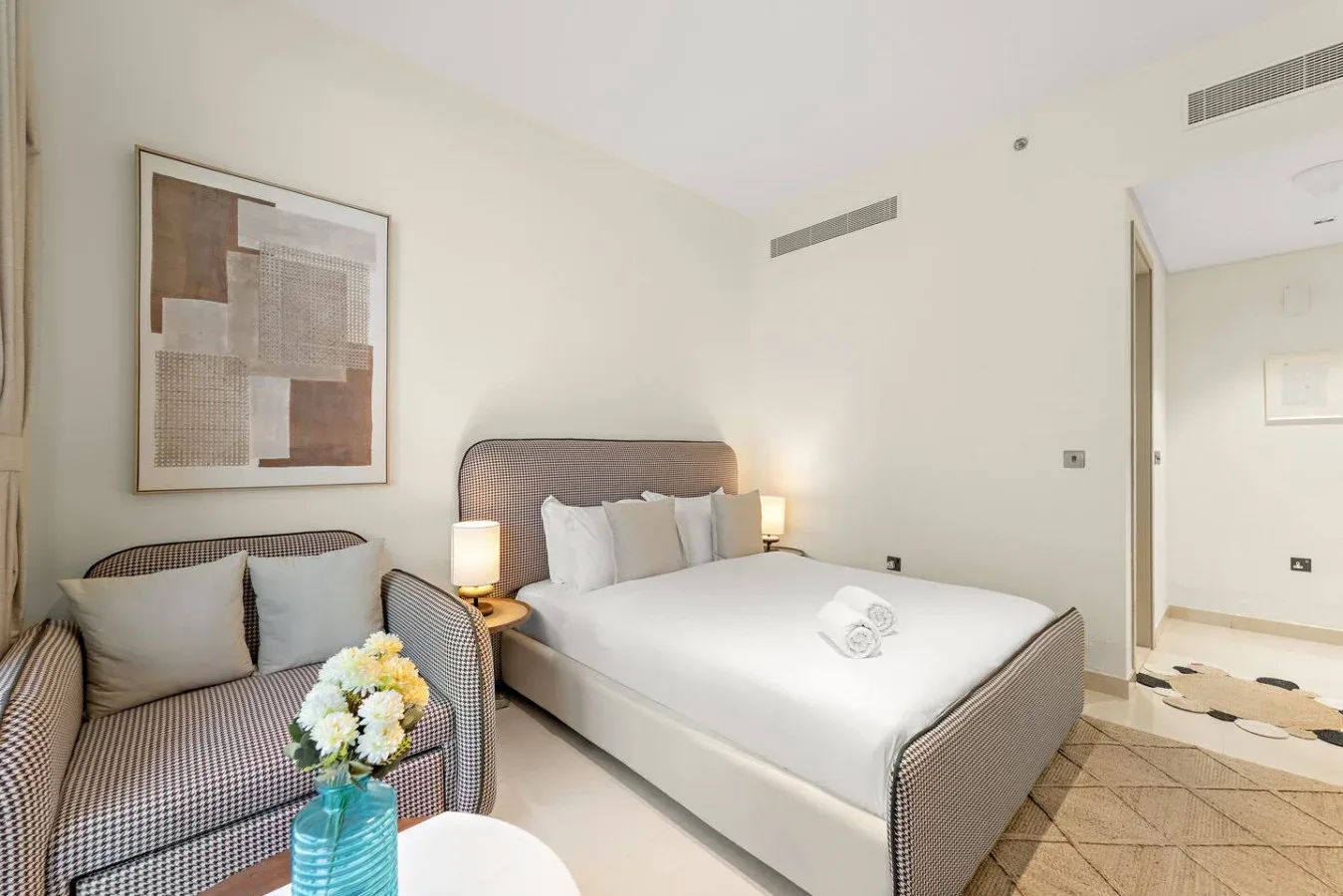 Un dormitorio luminoso con una cama bien tendida y asientos a un lado.