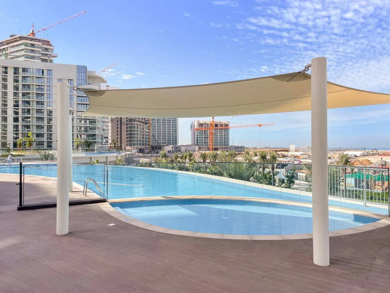 Una piscina al aire libre con una cubierta de sombra y edificios modernos al fondo.