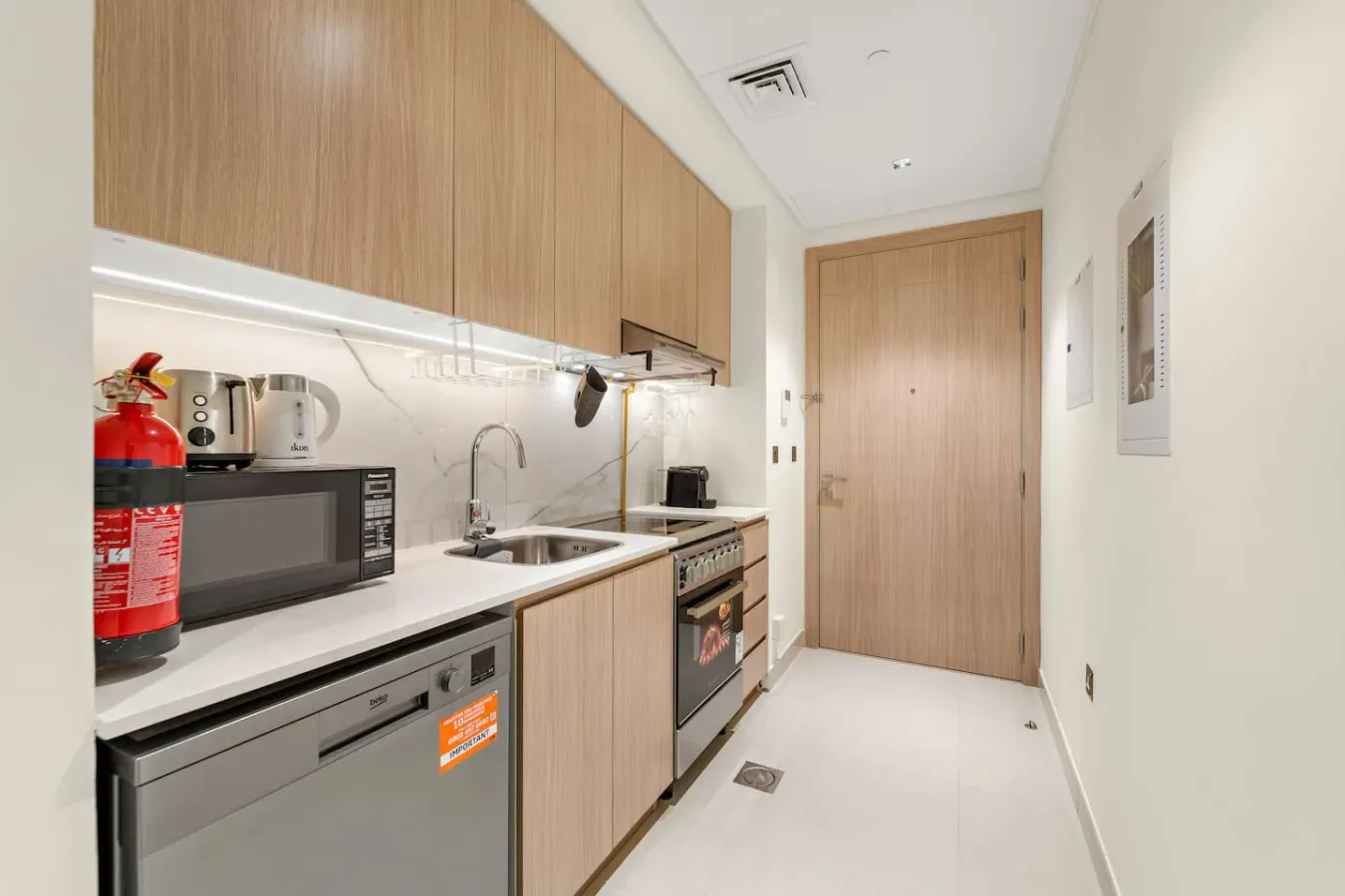 Una cocina compacta con gabinetes de madera clara, una encimera y electrodomésticos integrados.
