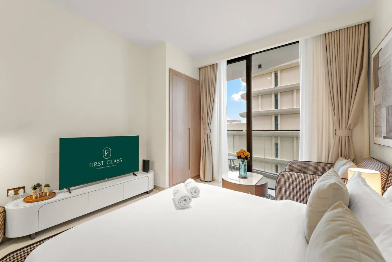 Un dormitorio luminoso con una cama grande, un televisor y una ventana con edificios a la vista.