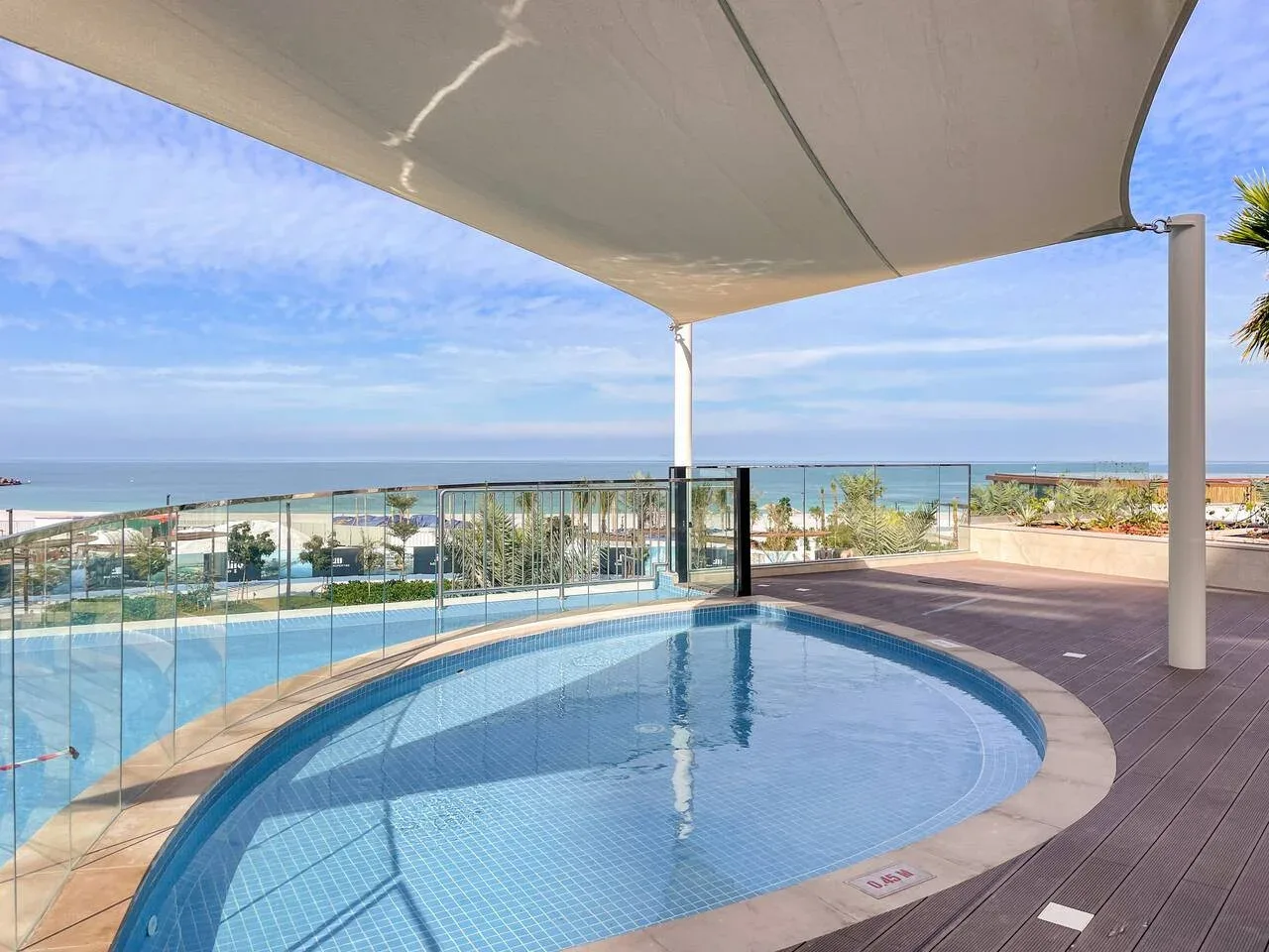 Una piscina exterior curva está junto a una terraza con vistas al mar.