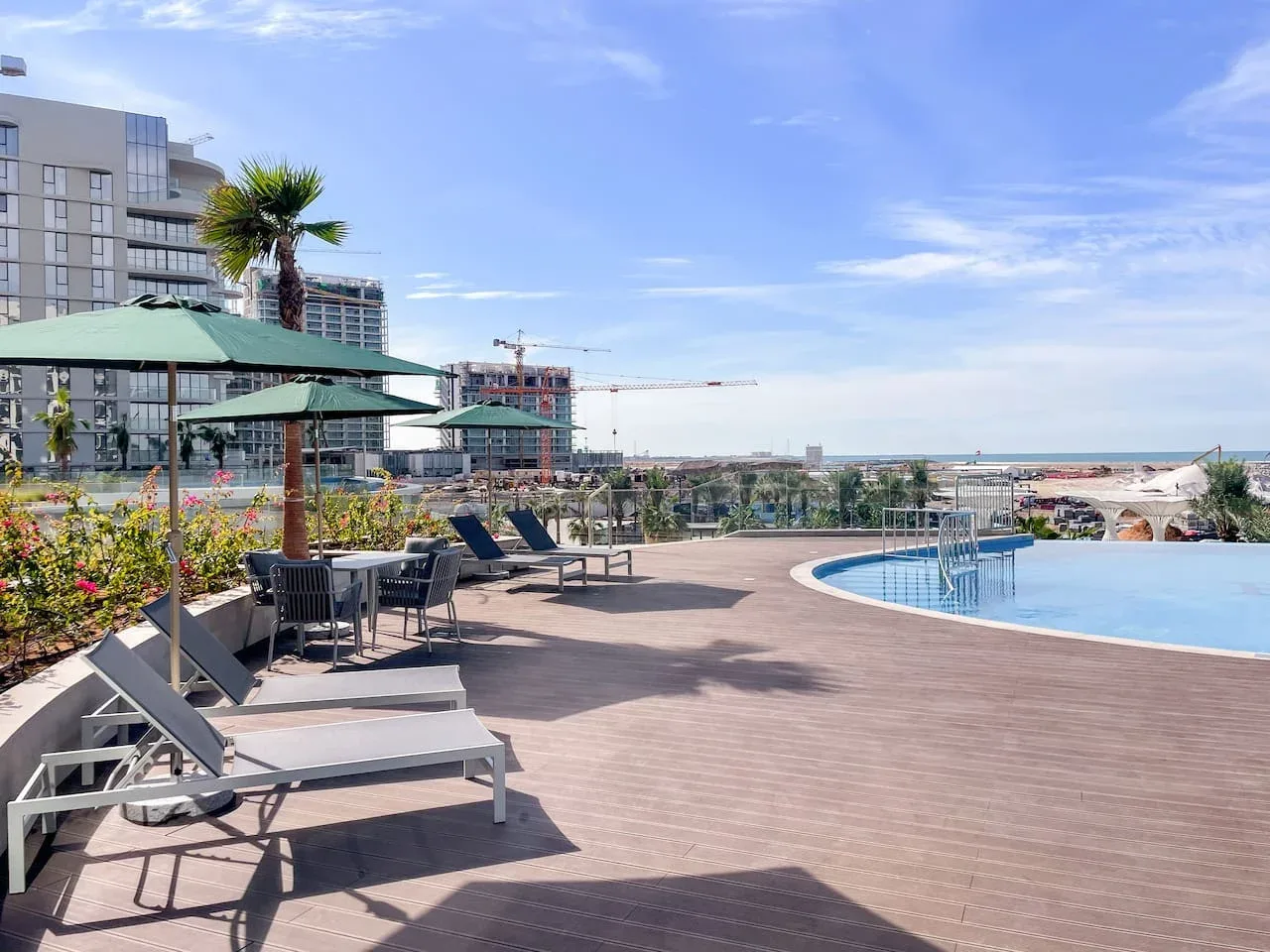 Una terraza con piscina, asientos reclinables, sombrillas y vistas de la costa cercana.