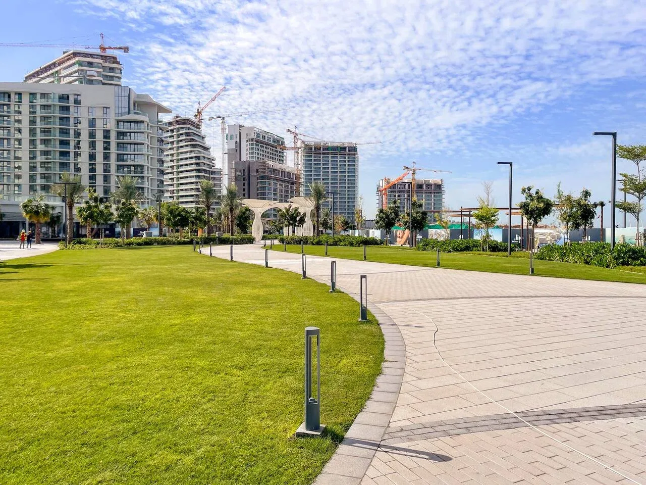 Un parque ajardinado con un camino pavimentado y edificios altos al fondo.