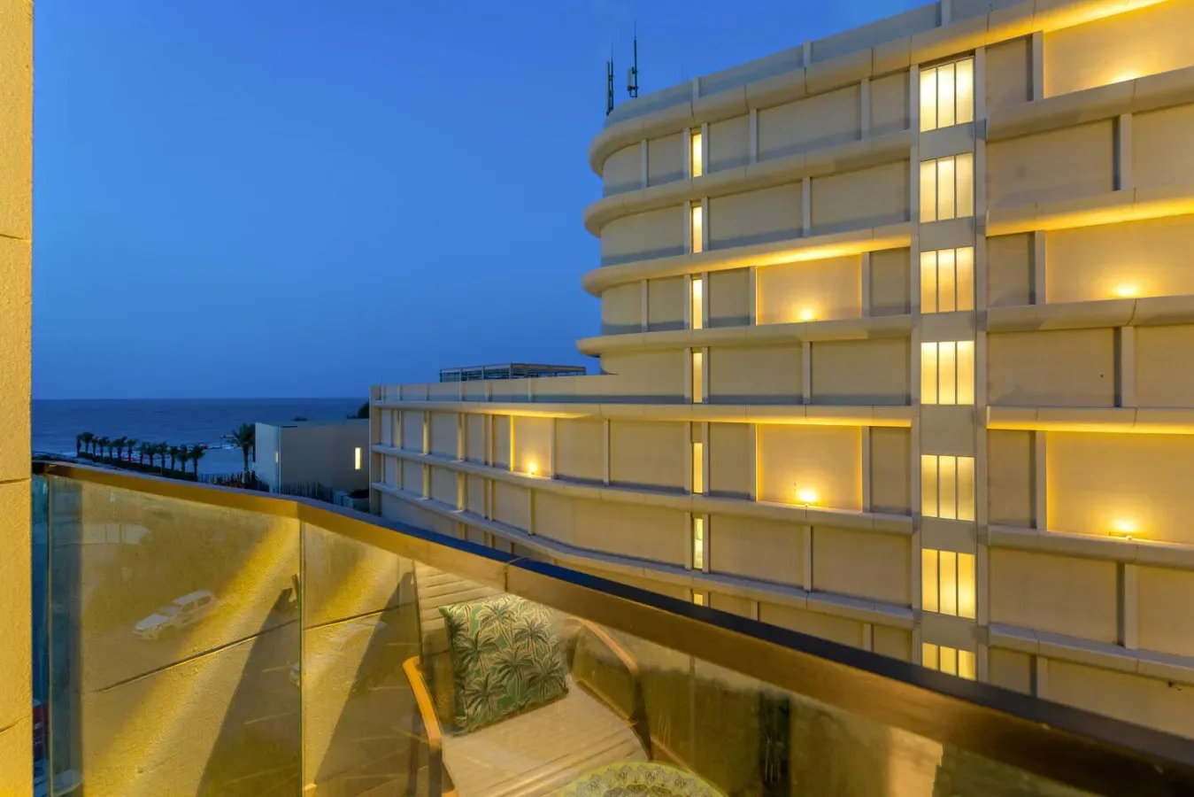 Un balcón con vistas al océano junto a un edificio moderno iluminado al anochecer.