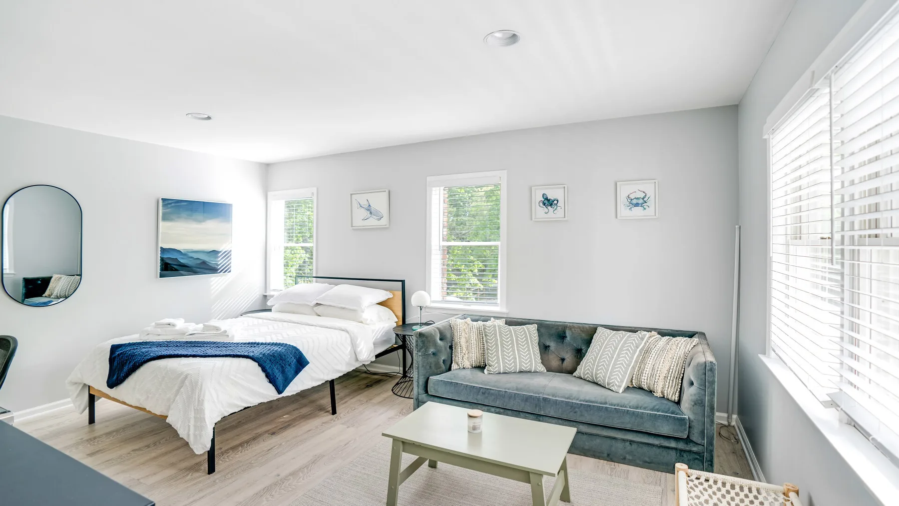 Un dormitorio luminoso con una cama bien tendida junto a un sofá azul.