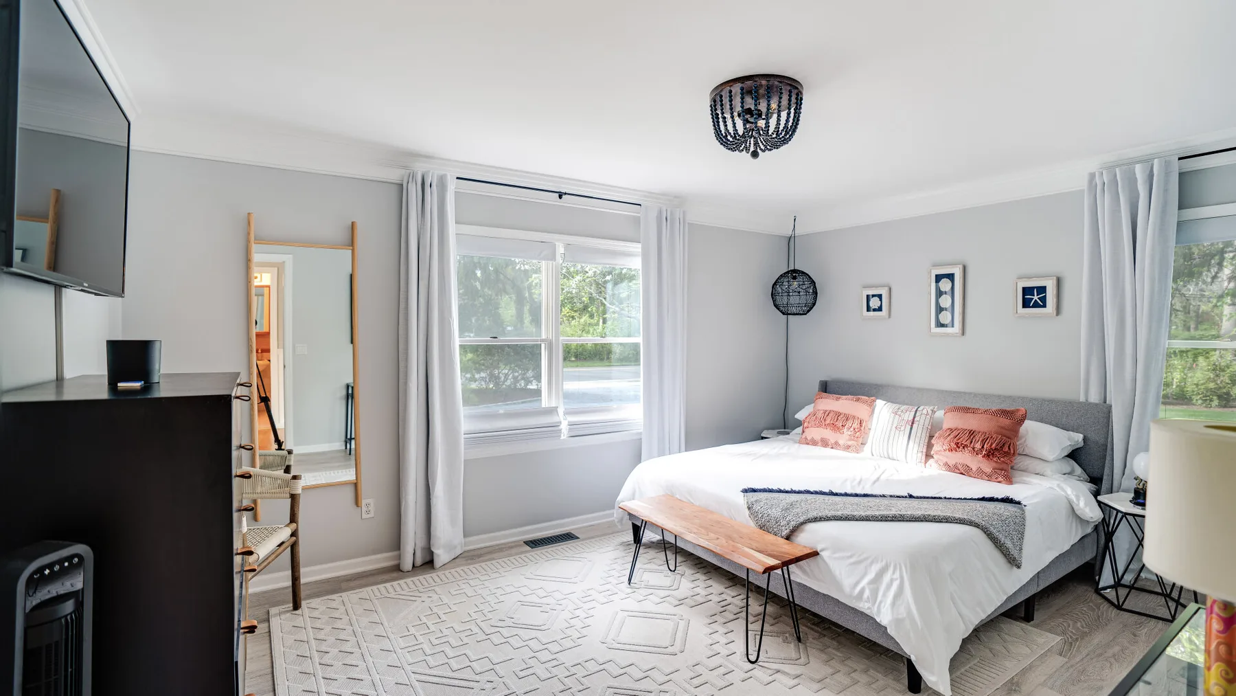 Un dormitorio con una cama, ventanas grandes y cortinas claras.