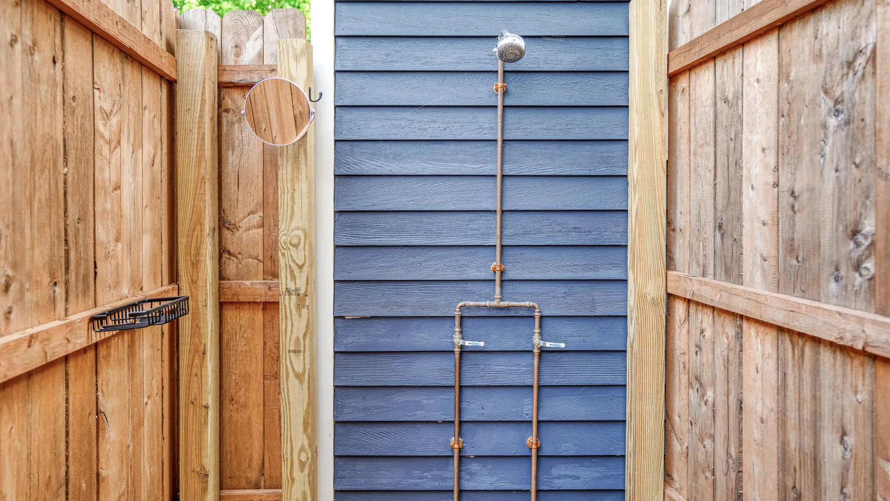 Una ducha exterior está frente a un revestimiento azul, entre paneles de madera.