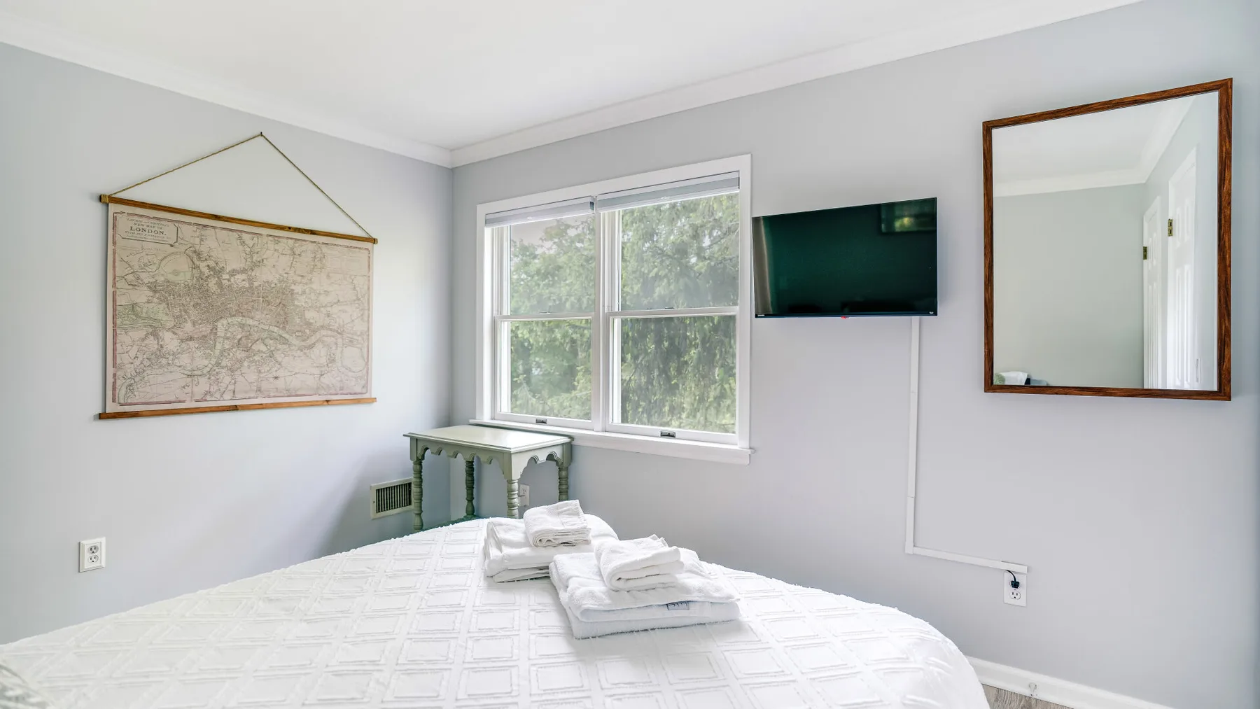Un dormitorio con una cama, toallas dobladas, una ventana y un televisor en la pared.
