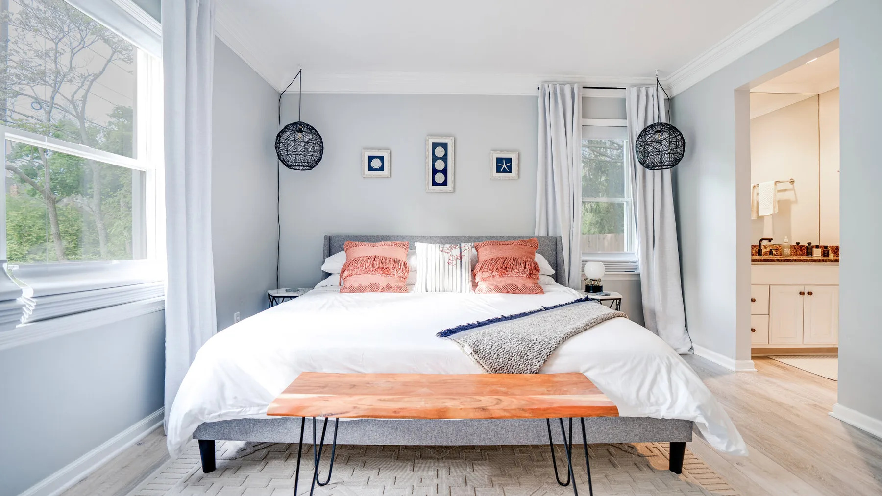 Un dormitorio luminoso con una cama, paredes claras y ventanas a ambos lados.