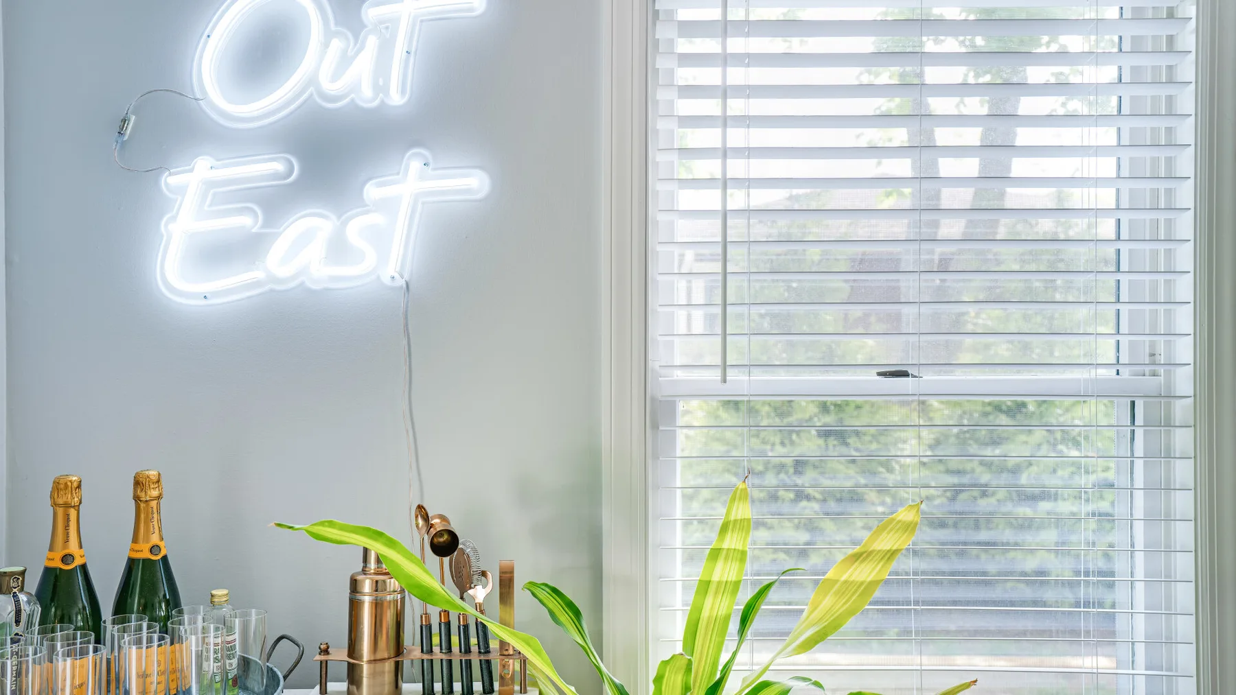 Un rincón interior luminoso con un letrero iluminado junto a una ventana con persianas.