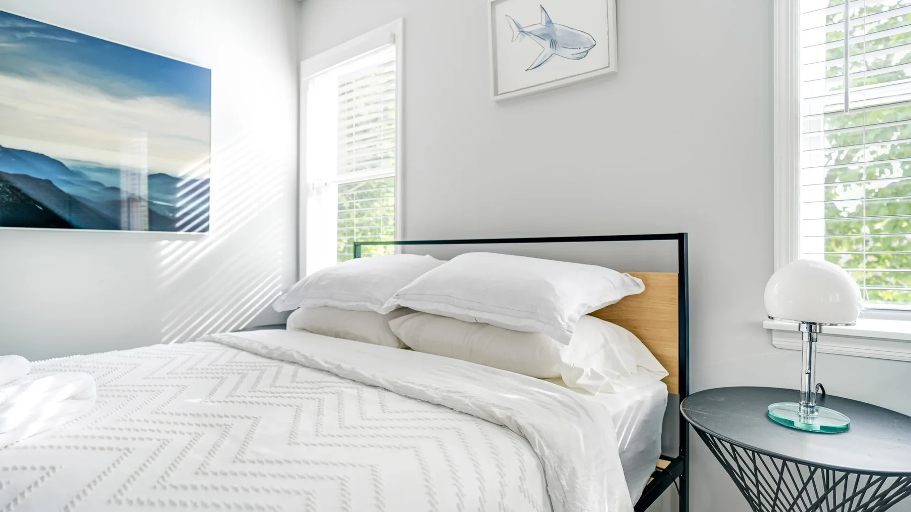 Un dormitorio luminoso con una cama tendida y cuadros enmarcados.