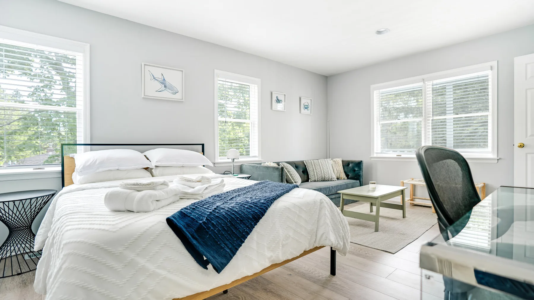 Un dormitorio luminoso con una cama bien tendida y grandes ventanas.