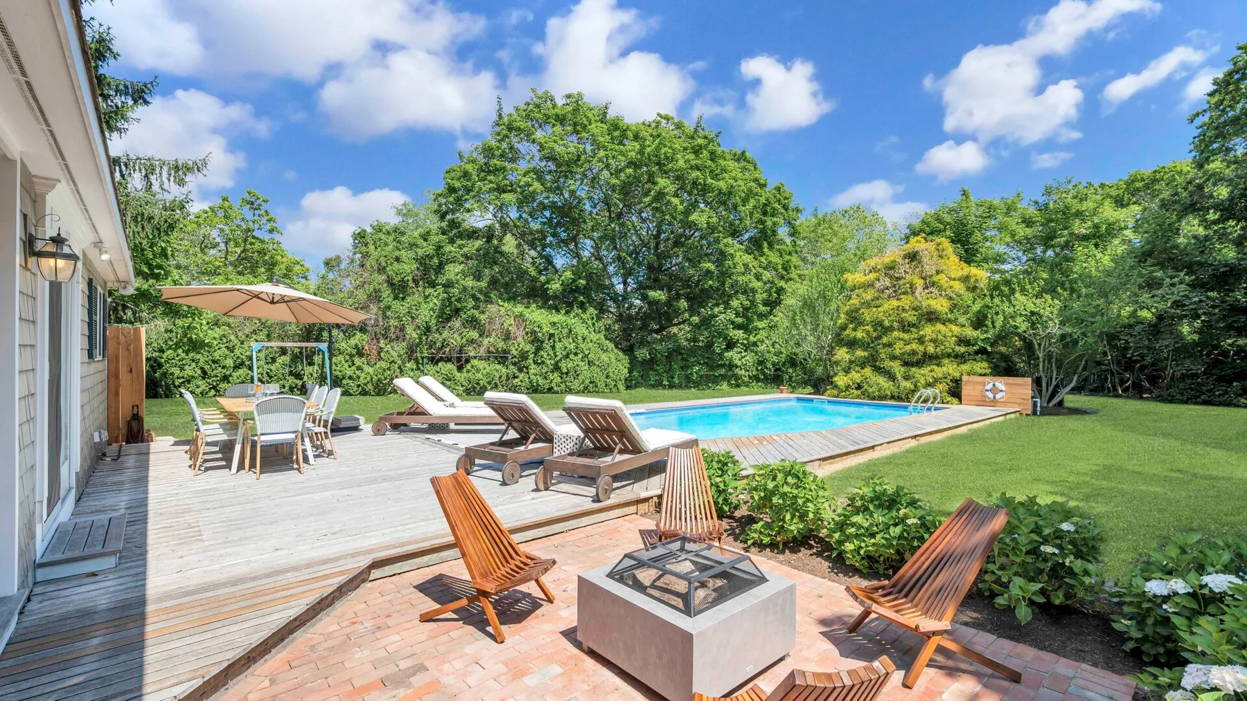 Outdoor patio with seating, a swimming pool, and a fire pit beside a green lawn.