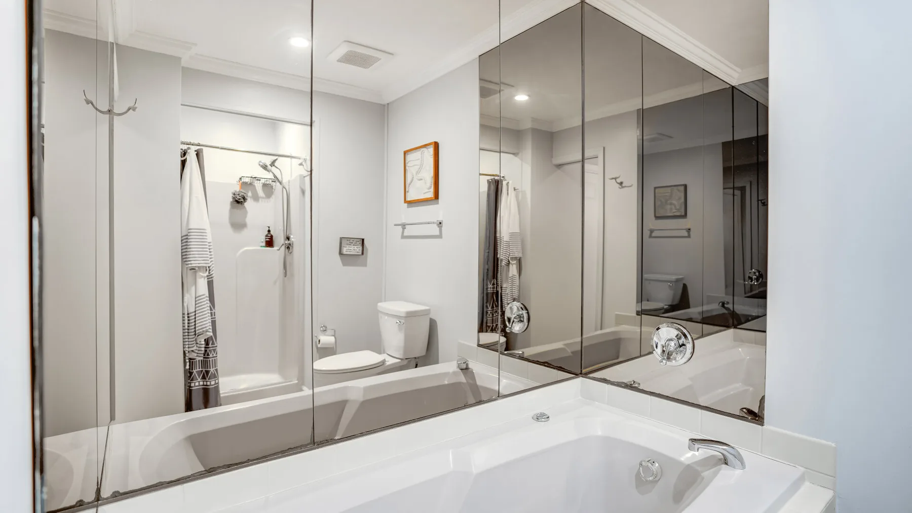 Un baño luminoso con bañera, ducha y grandes paredes de espejo.